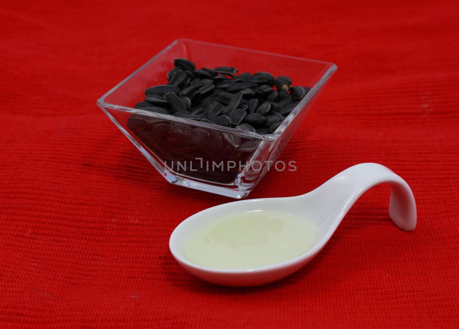 sunflower seeds in the bowl and oil over red background
