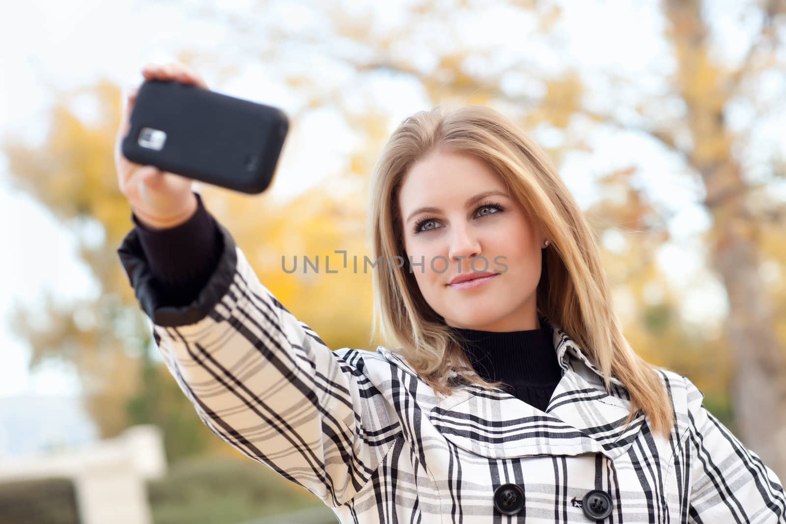 Pretty Young Woman Taking Picture with Camera Phone in the Park One Fall Day.