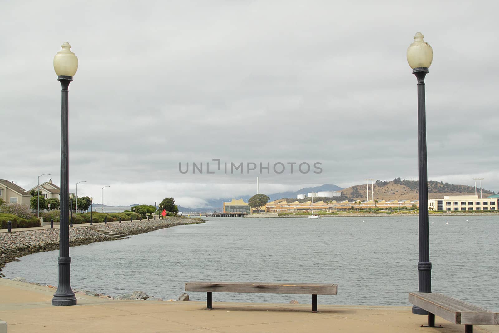 Two street lamps and a bench on pier on cloudy day