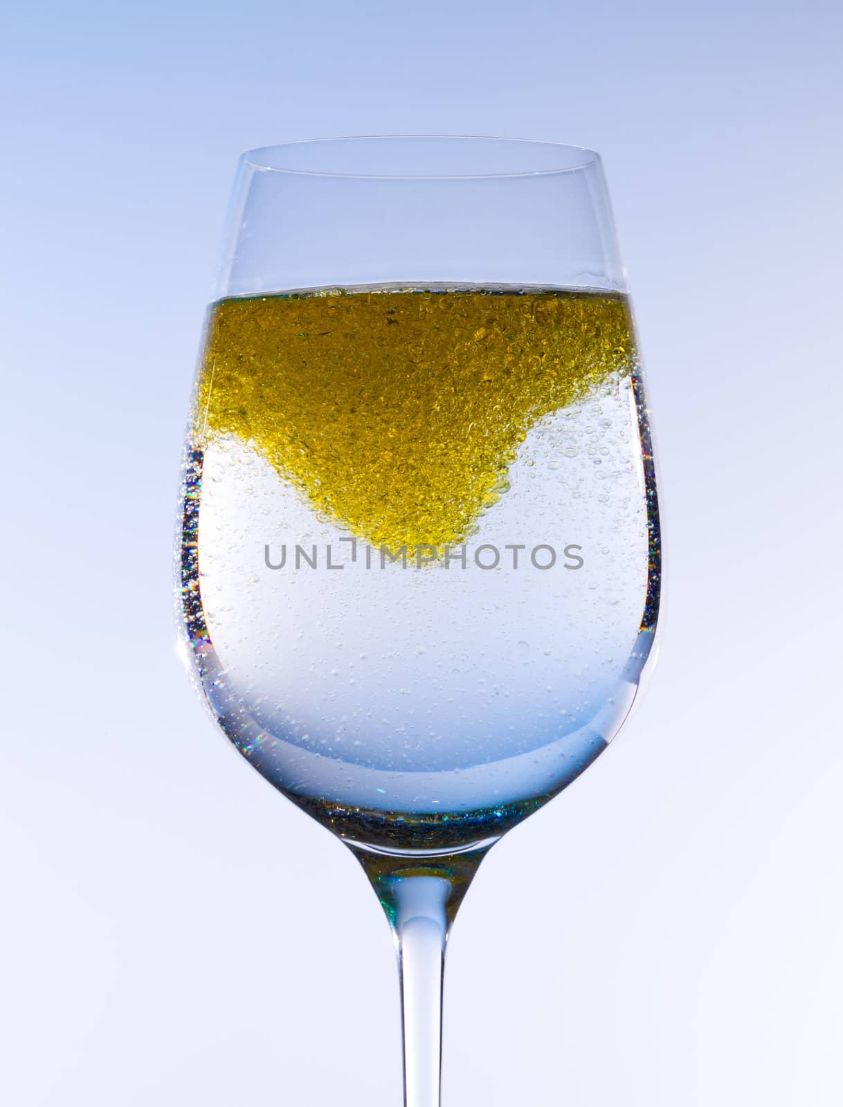 Olive oil being stirred in a large wine goblet forming golden bubbles in the liquid