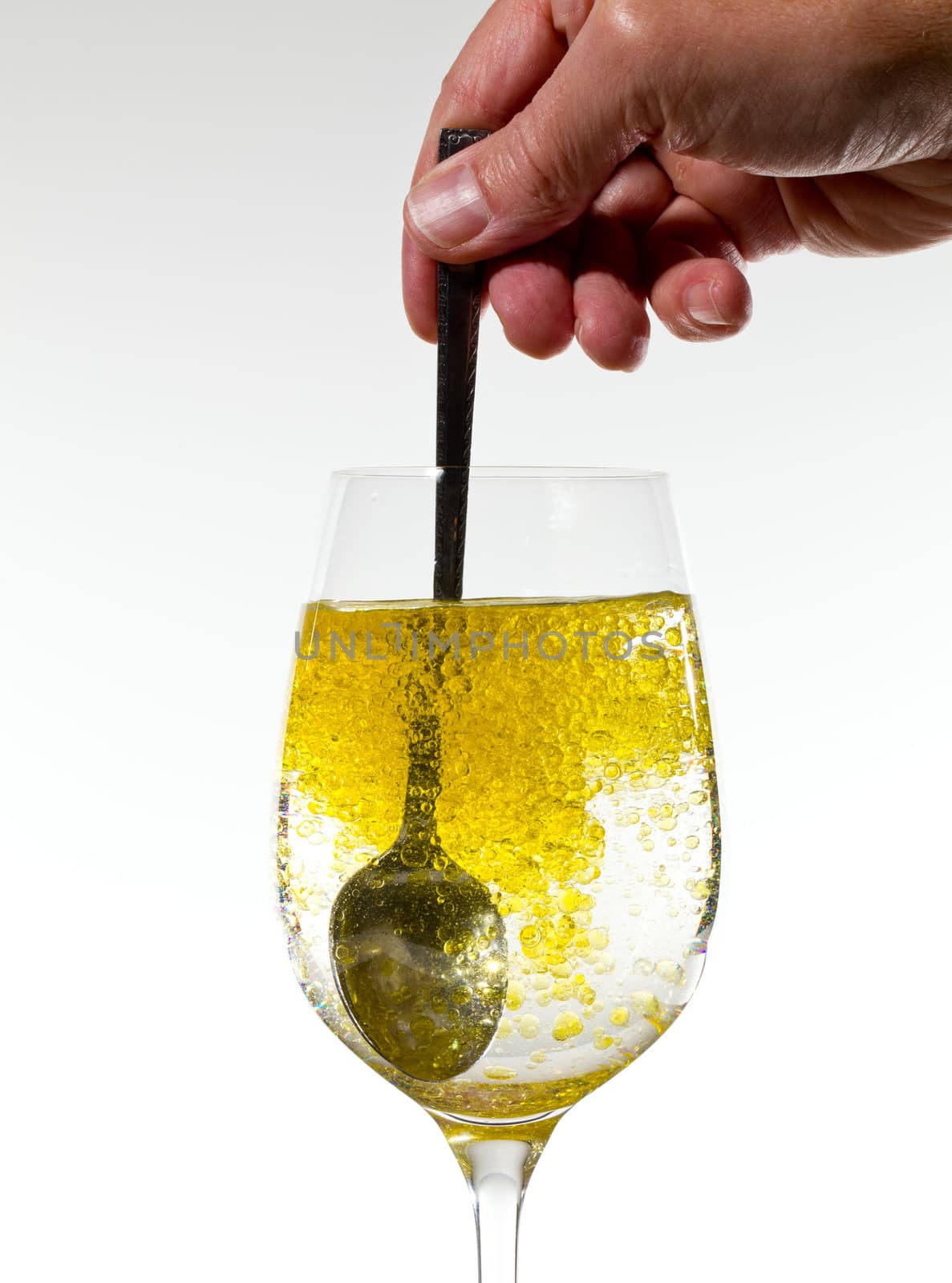 Olive oil being stirred in a large wine goblet forming golden bubbles in the liquid