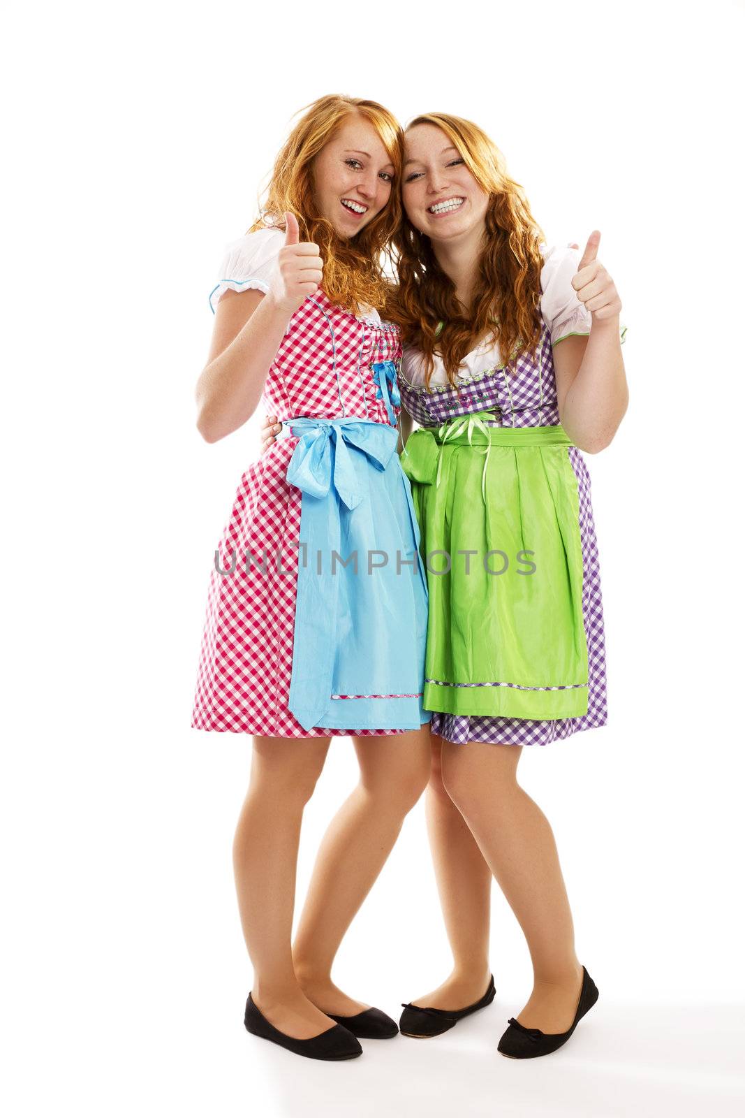 two happy bavarian dressed girls showing thumbs up on white background