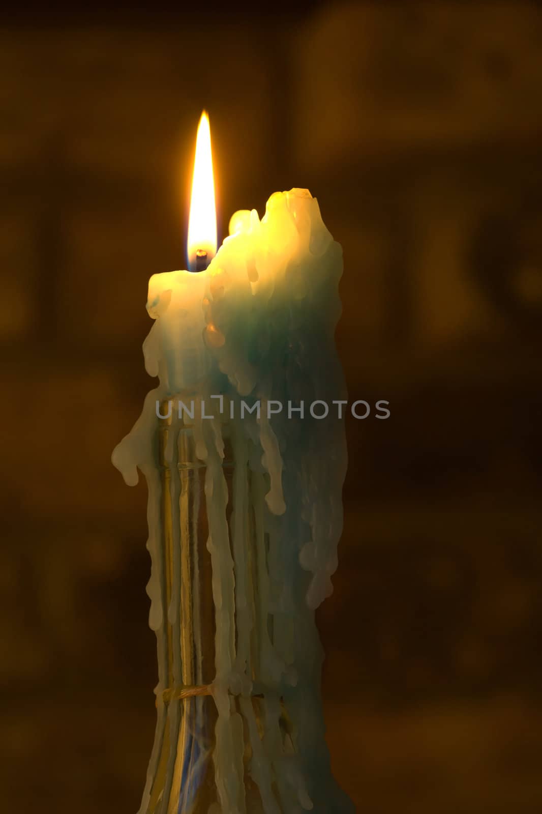 A candle burns in a bottle with a wax build up.