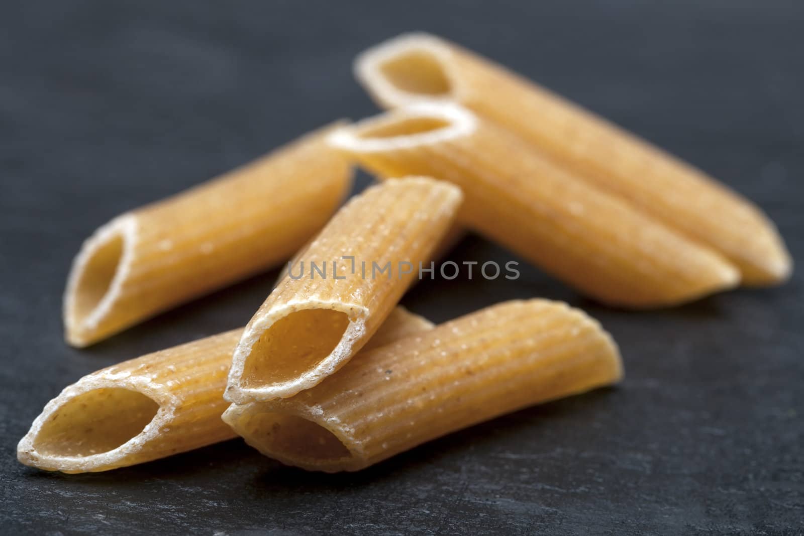 Closeup of dried penne on stone surface.