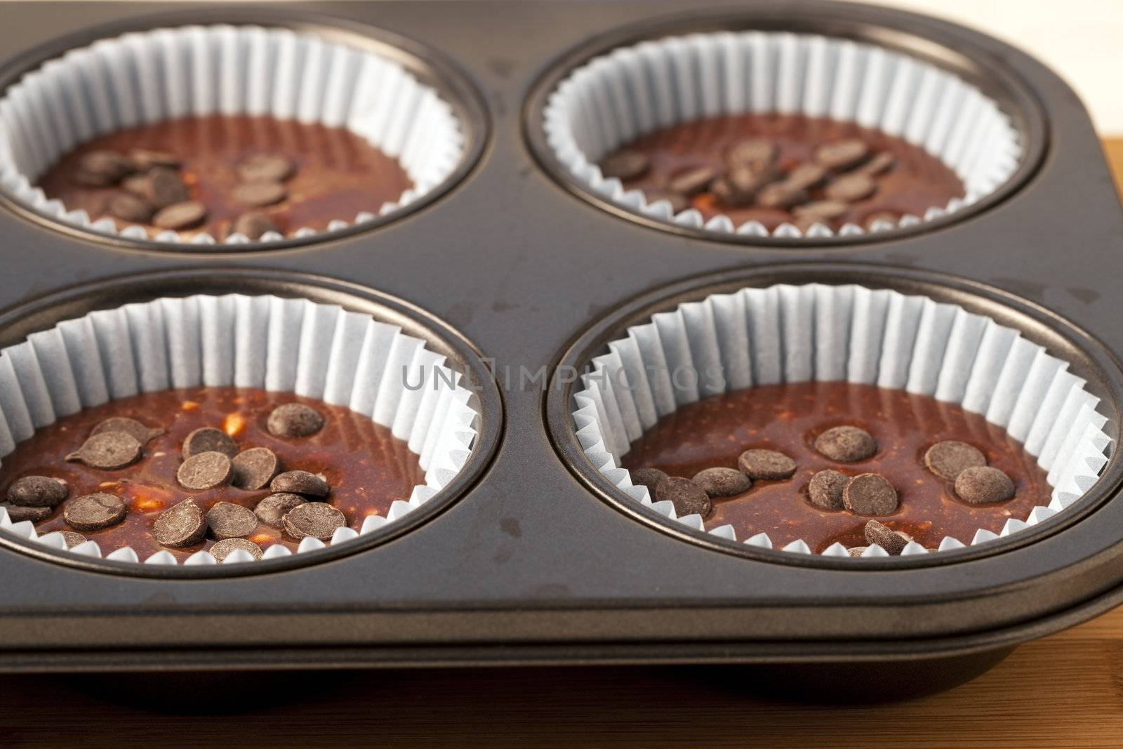 Muffin pan with chocolate batter and chocolate chips.