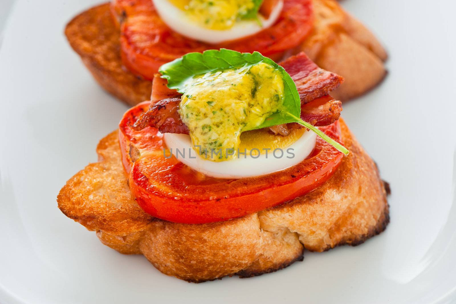 A baguette slice with tomato egg bacon and herb butter
