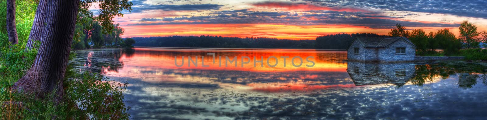 Panorama of a sunrise and pump house utility on a lake.