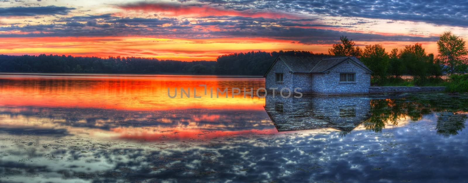 Panorama of a sunrise and pump house utility on a lake.