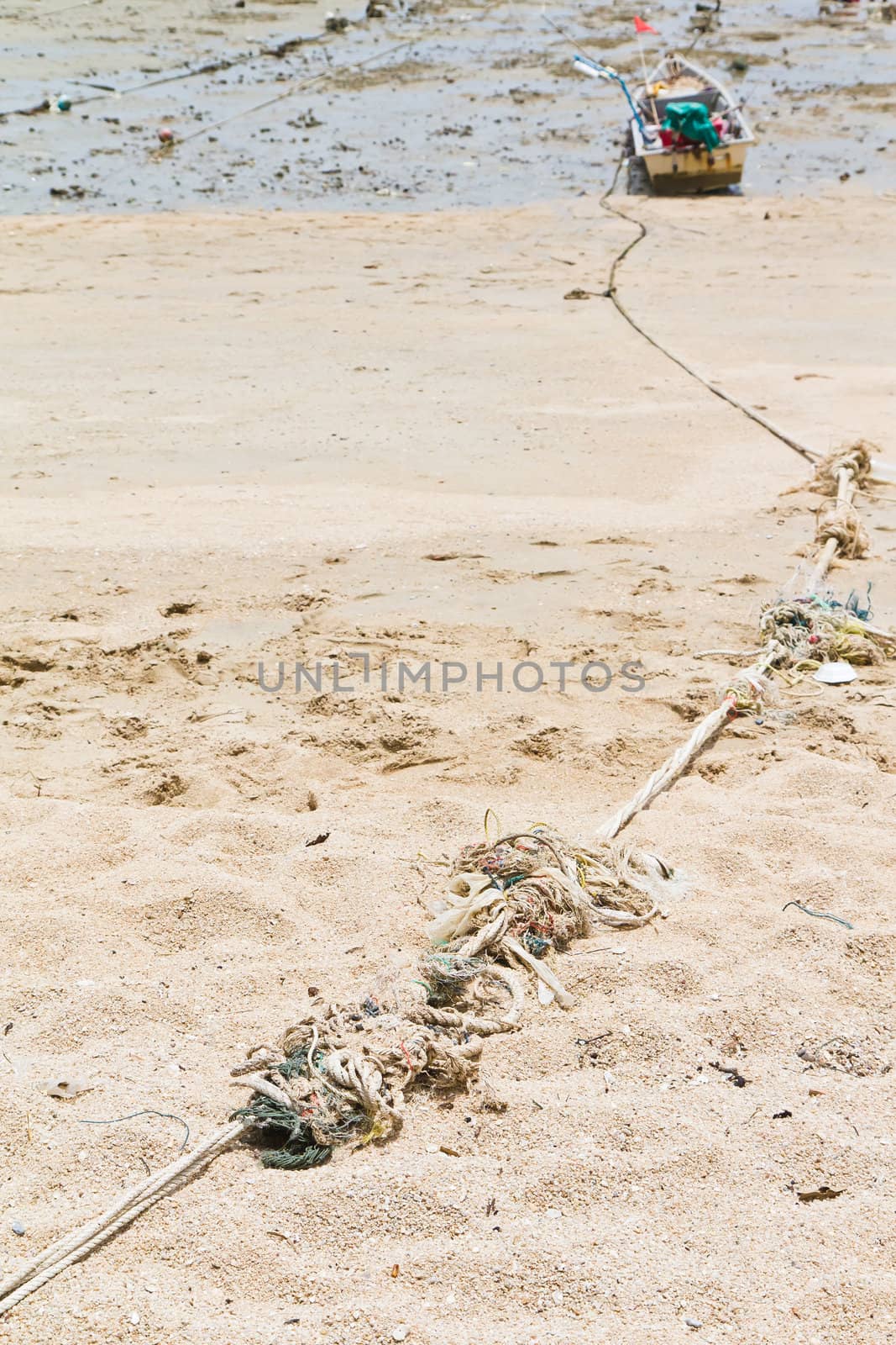 Rope tied to a fishing boat on the beach near the ocean in view.