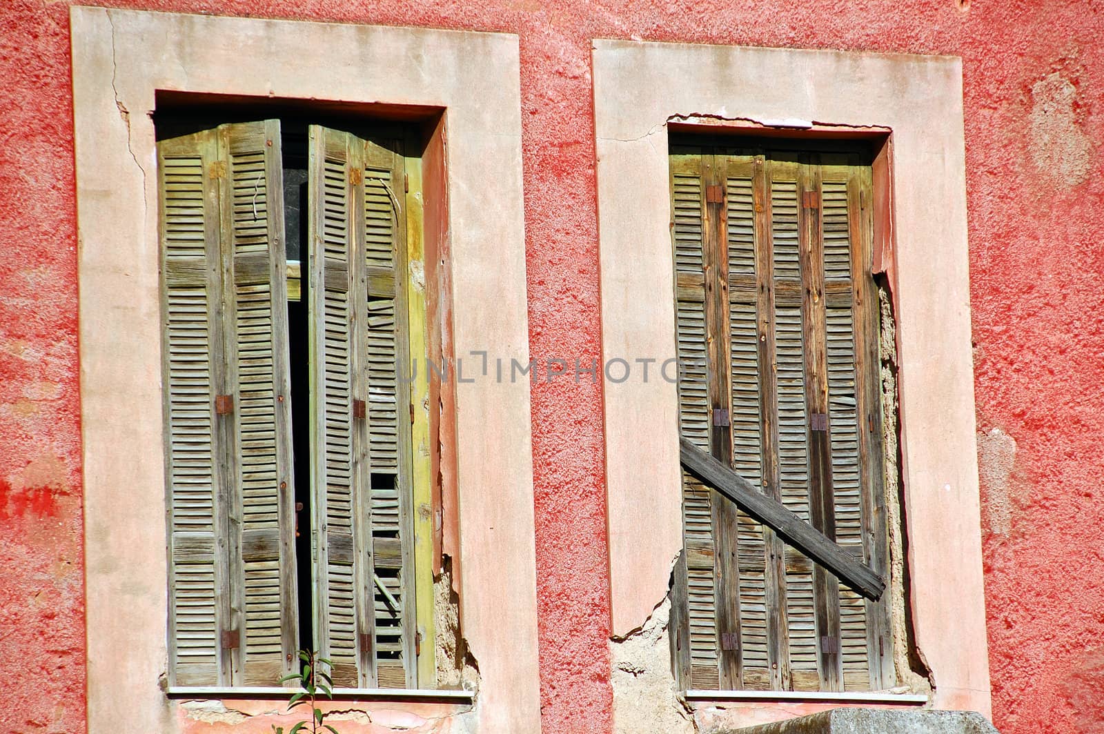 Boarded up window shutters and weathered red wall. Abandoned house detail.