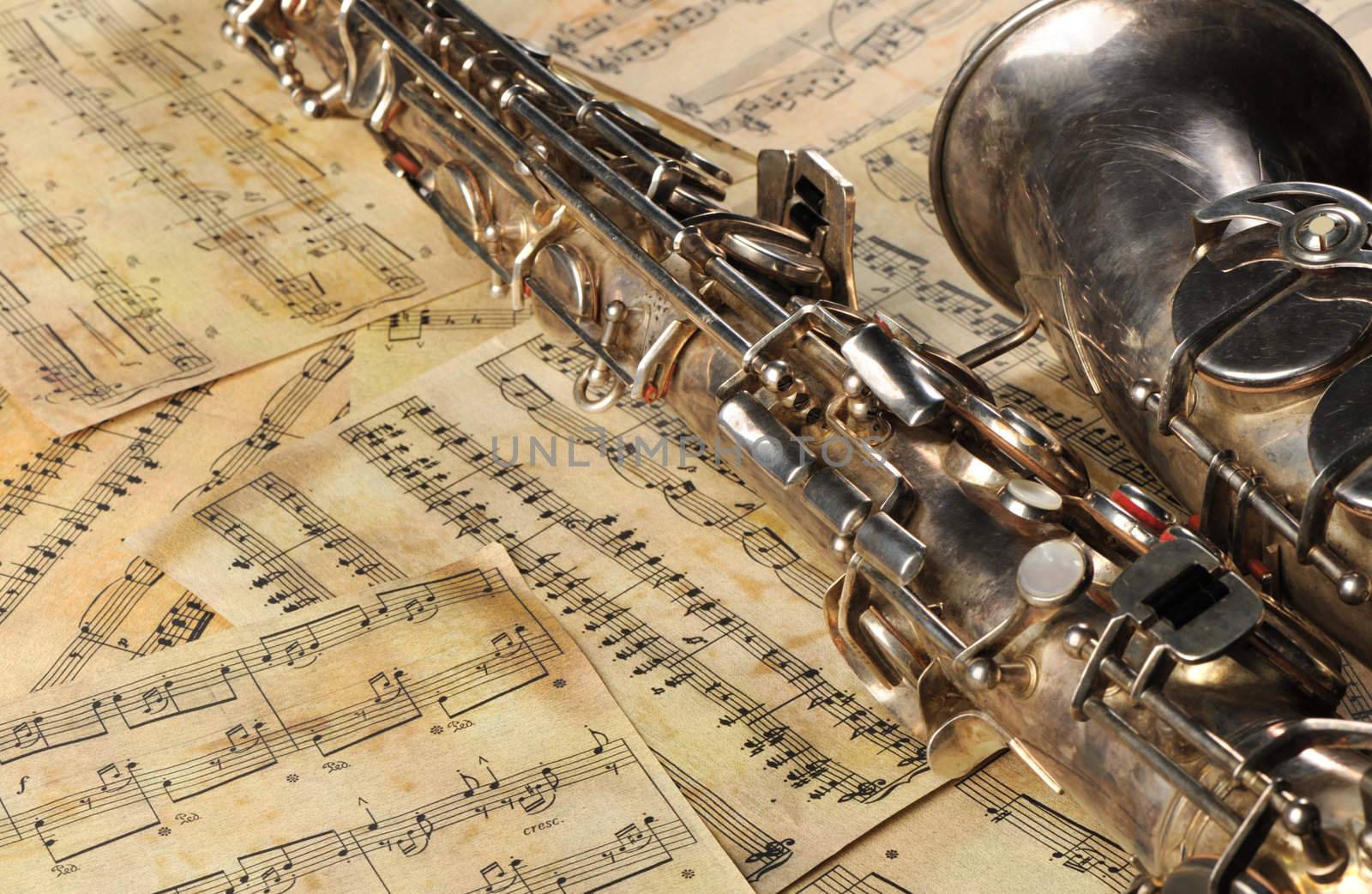Old saxophone and notes. The Musical instrument laying on notes with classical music of the beginning of 17 centuries