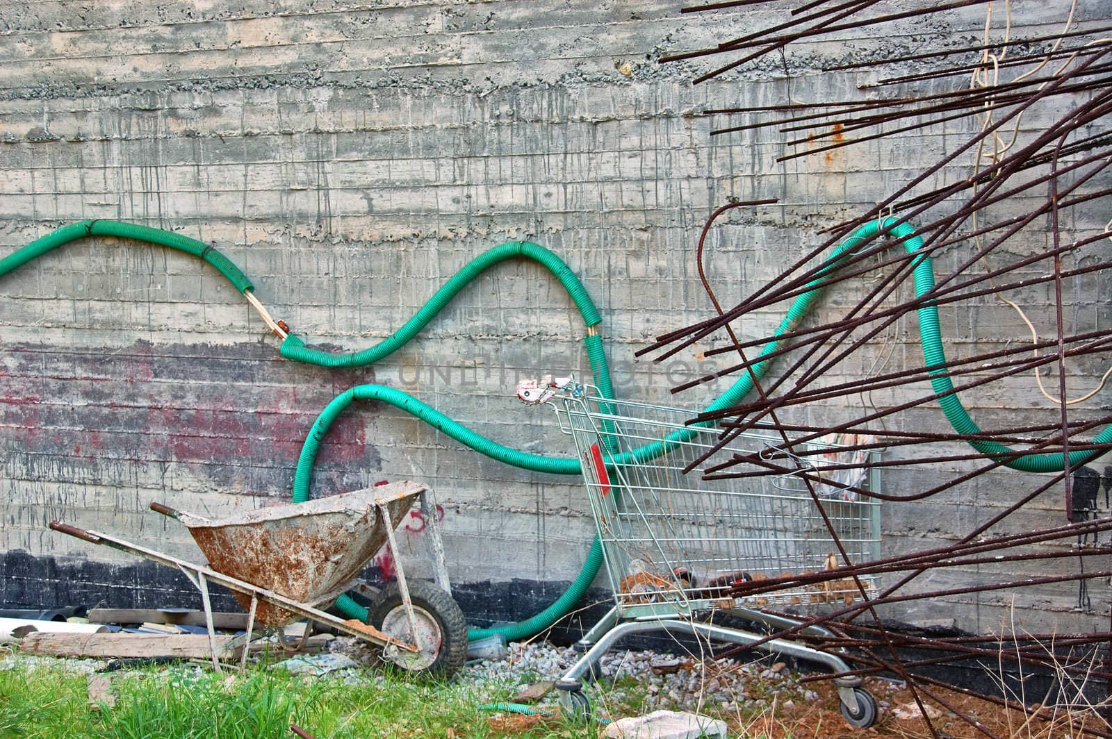 Concrete stained wall at construction site. Wheelbarrow, cart and metal bars.