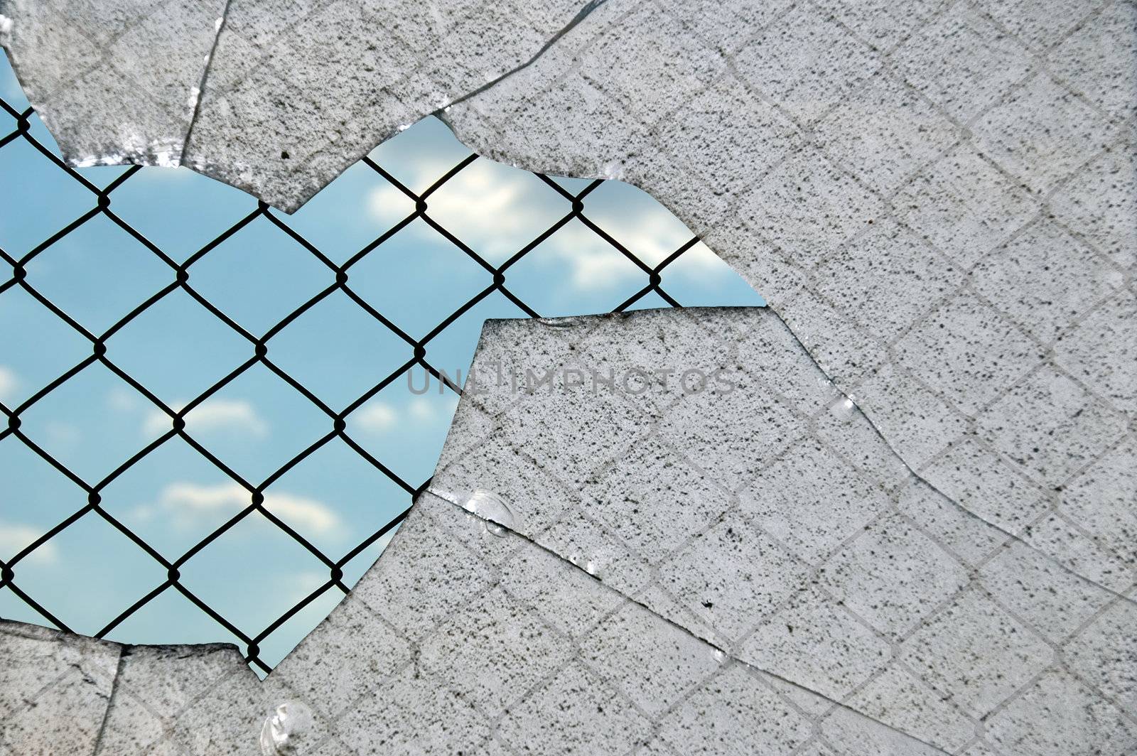 Broken glass fragments and chain link wired fence pattern against blue sky.