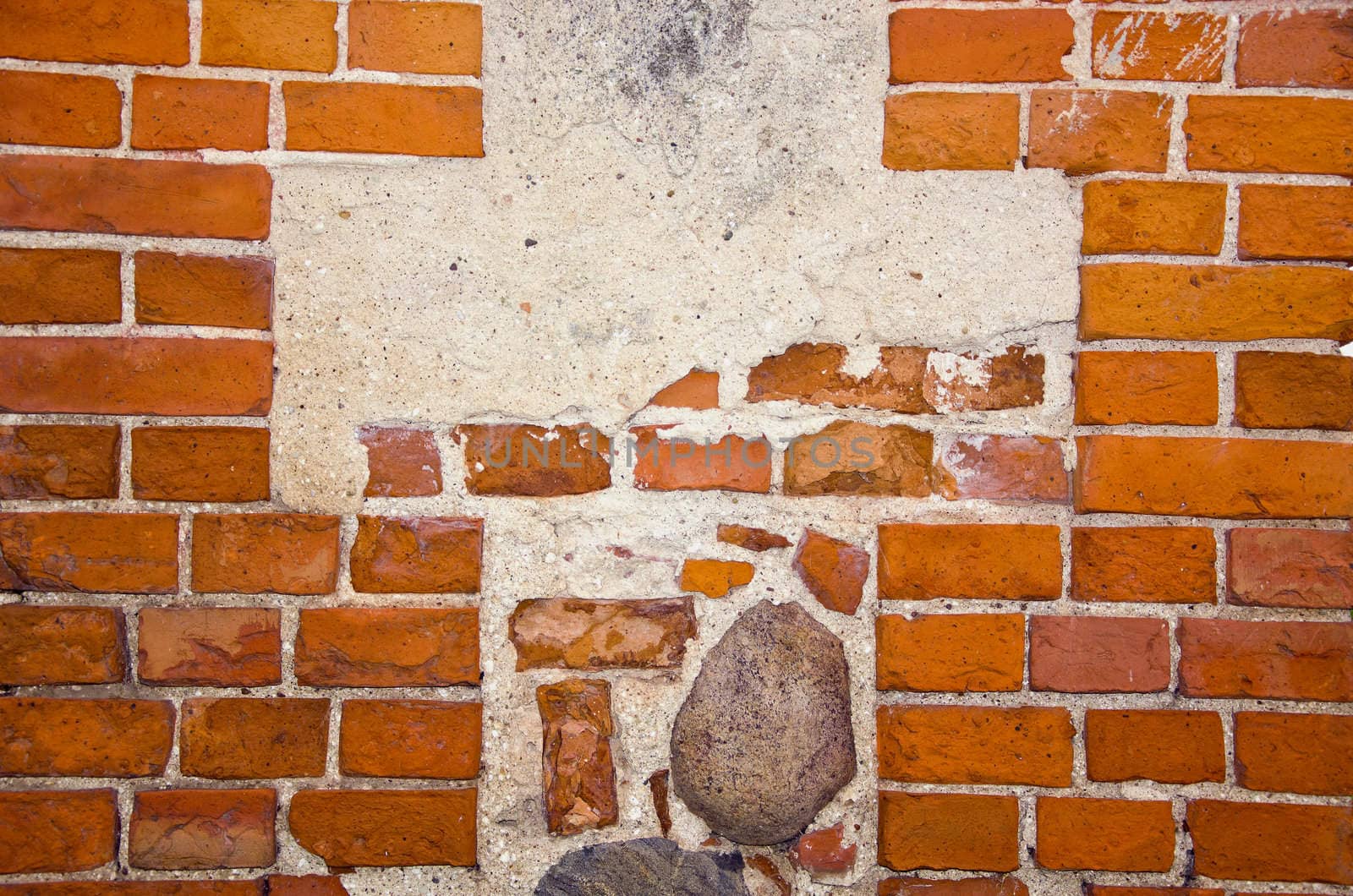 Fragment of ancient red brick wall with stones ant cement in it.