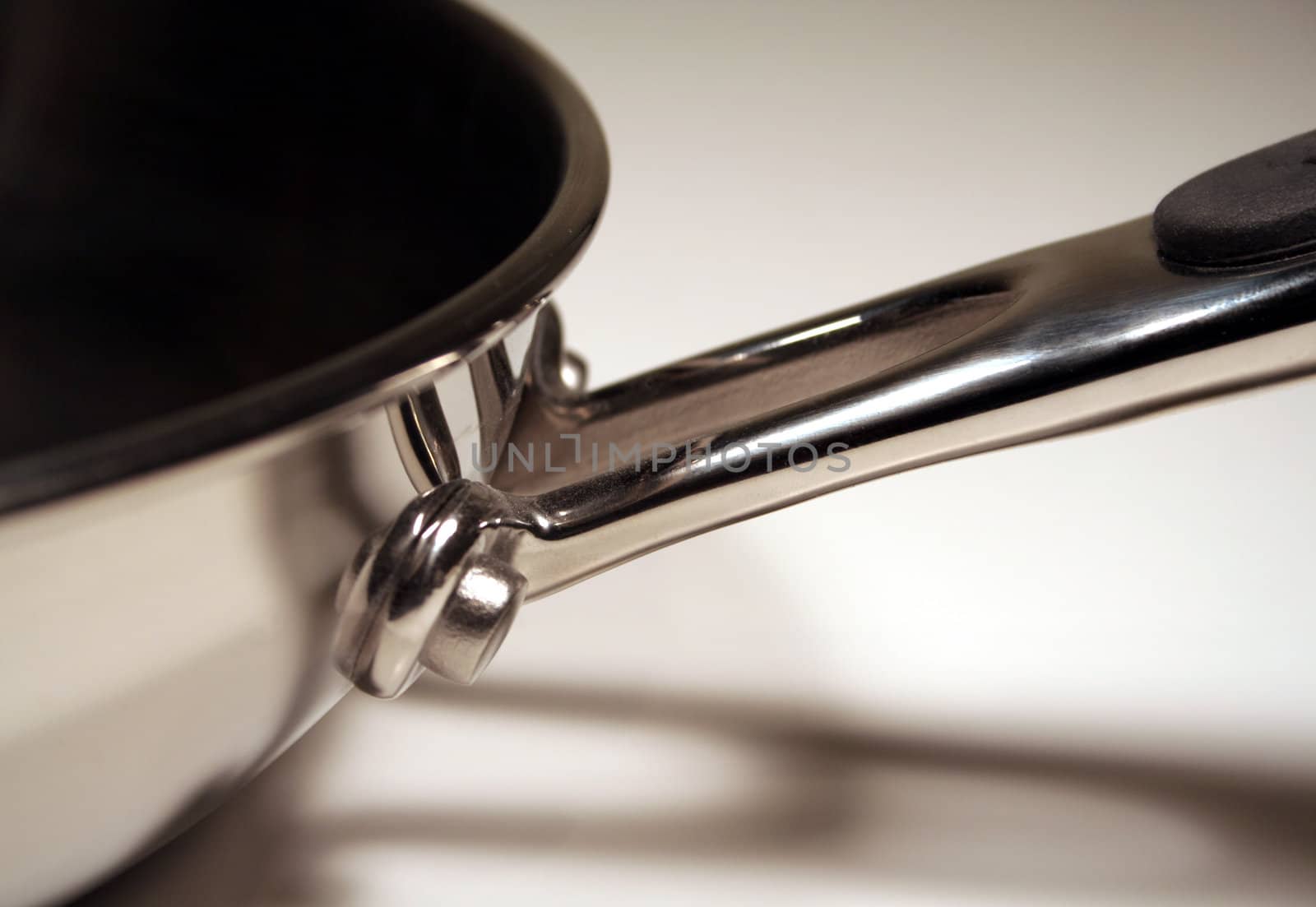 A close up of the handle of a stainless steel frying pan.