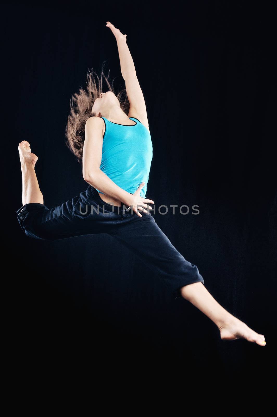 Young woman in tracksuit jumping on black background