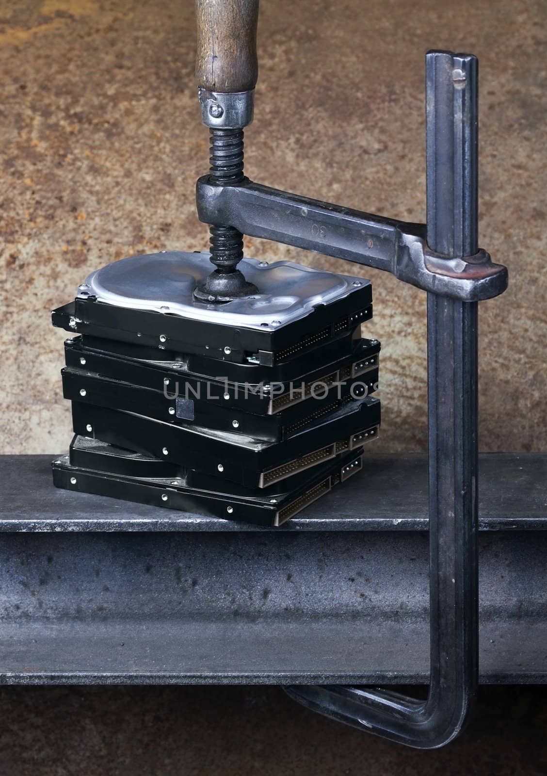 heavy screw clamp giving pressure to several hard drives. Studio shot taken in front of rusty background
