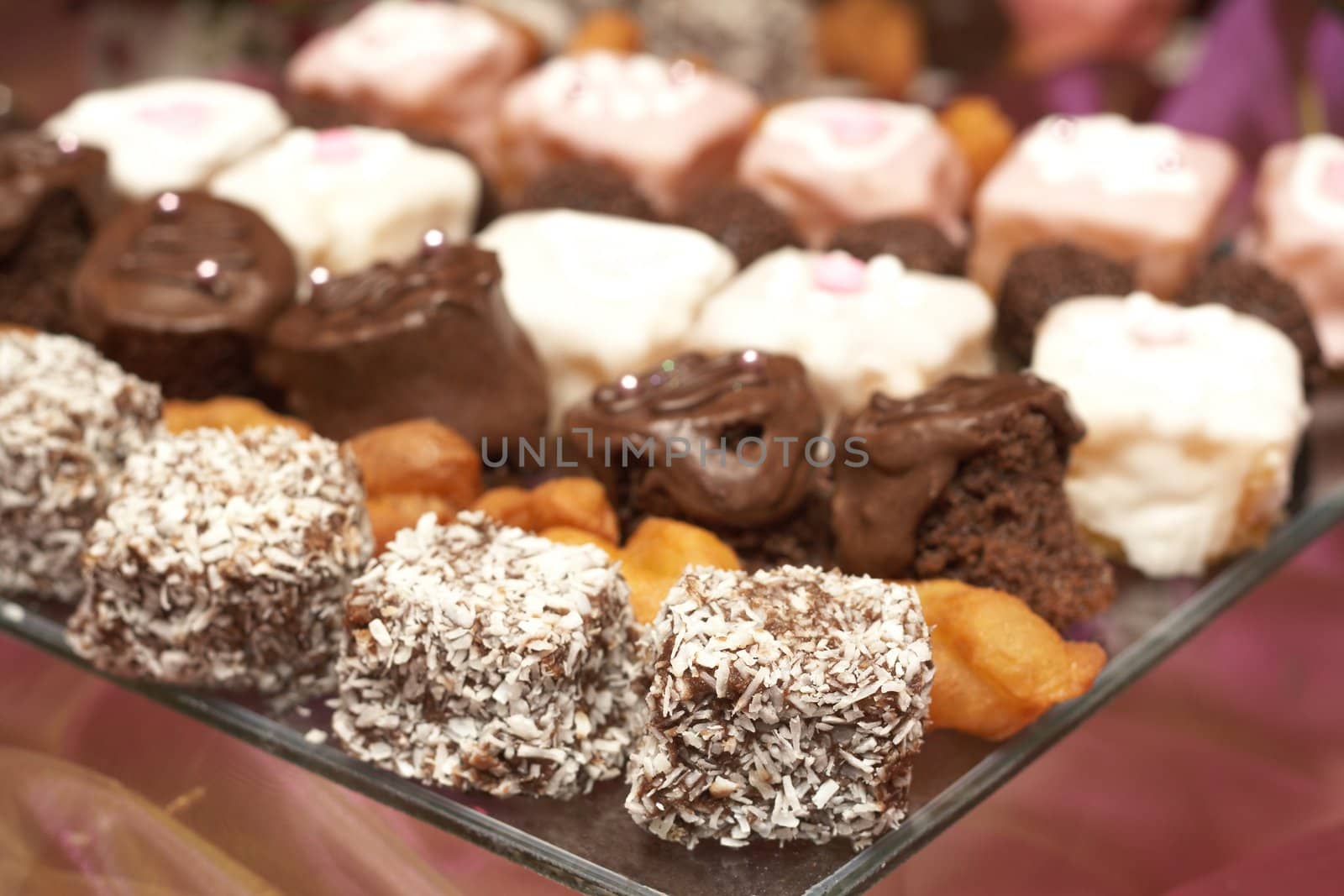 Selection of miniature petit-fours - coconut, chocolate cream, strawberry and vanilla cakes on glass plate