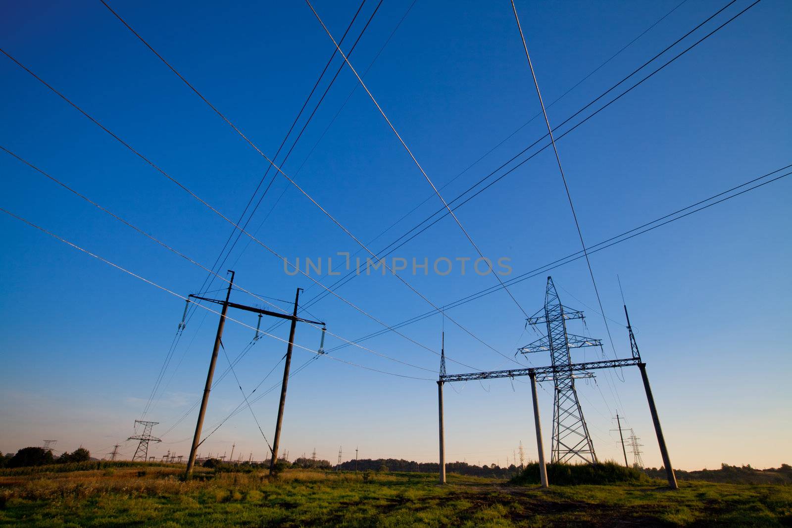 Electric power lines in a field over blue morning sky with many crossing wires. Horizontal