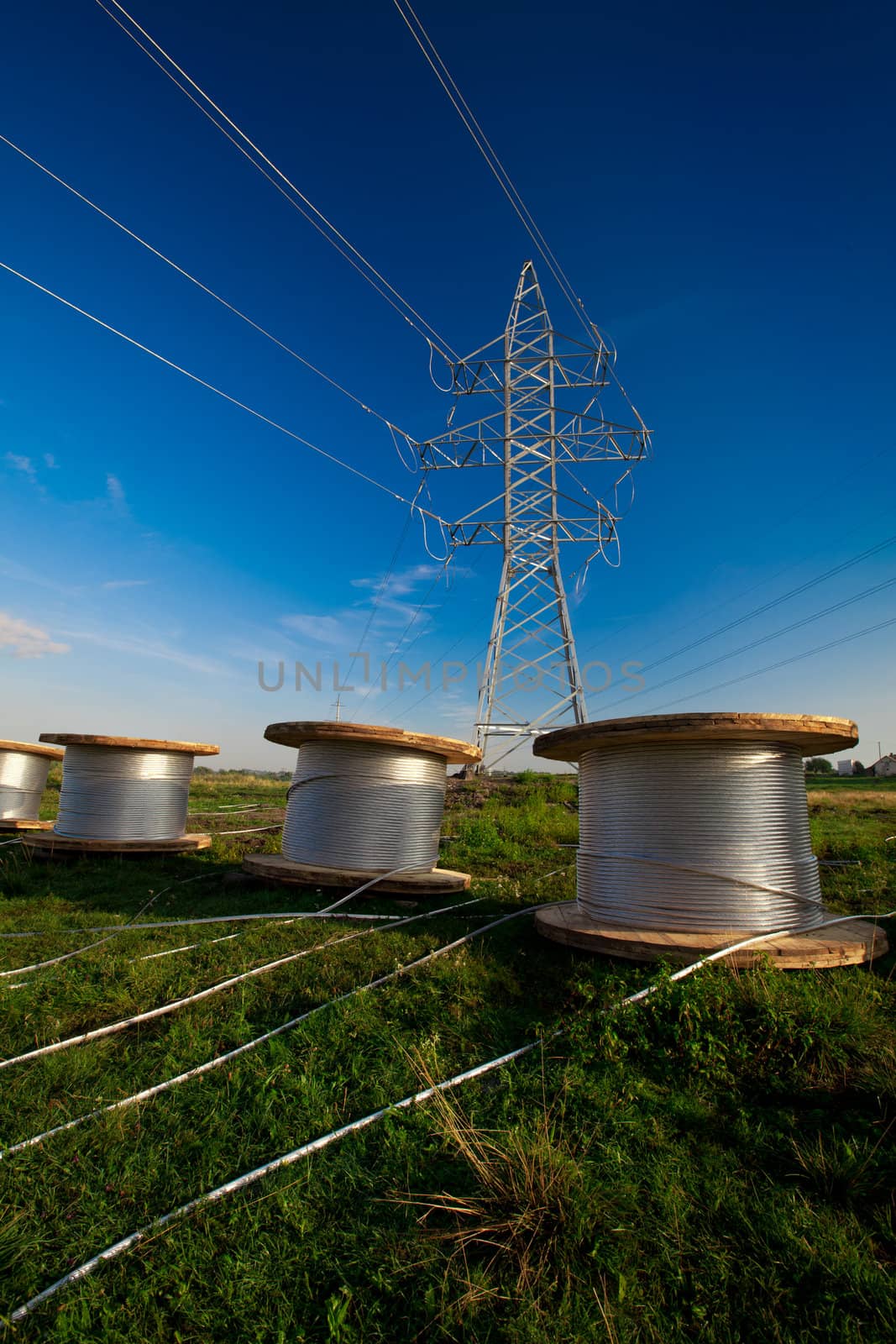 A power line tower in the field and bobbins with aluminum wire ready to installation