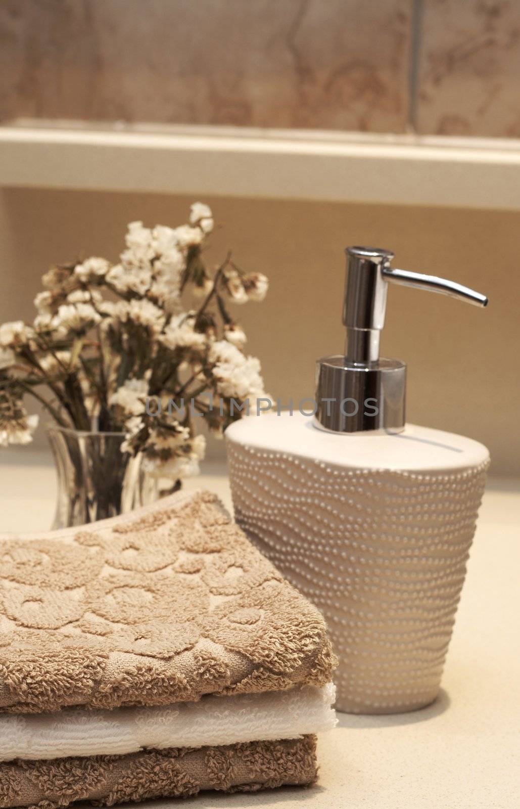 Stack of white and brown towels and bottle of liquid soap with some dry flowers in the bathroom