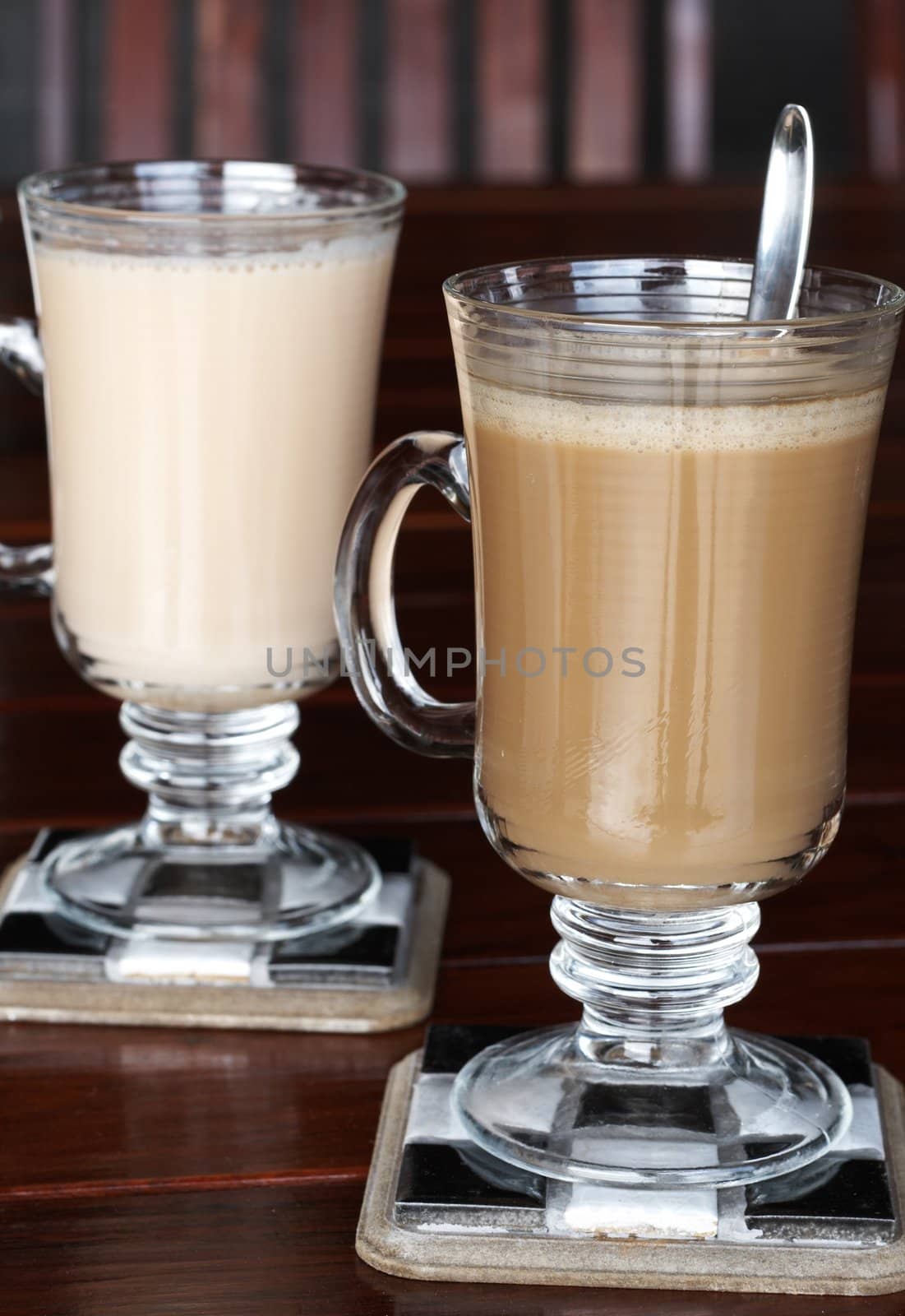 Closeup of coffee and tea with milk in glass cups on cherry wood table