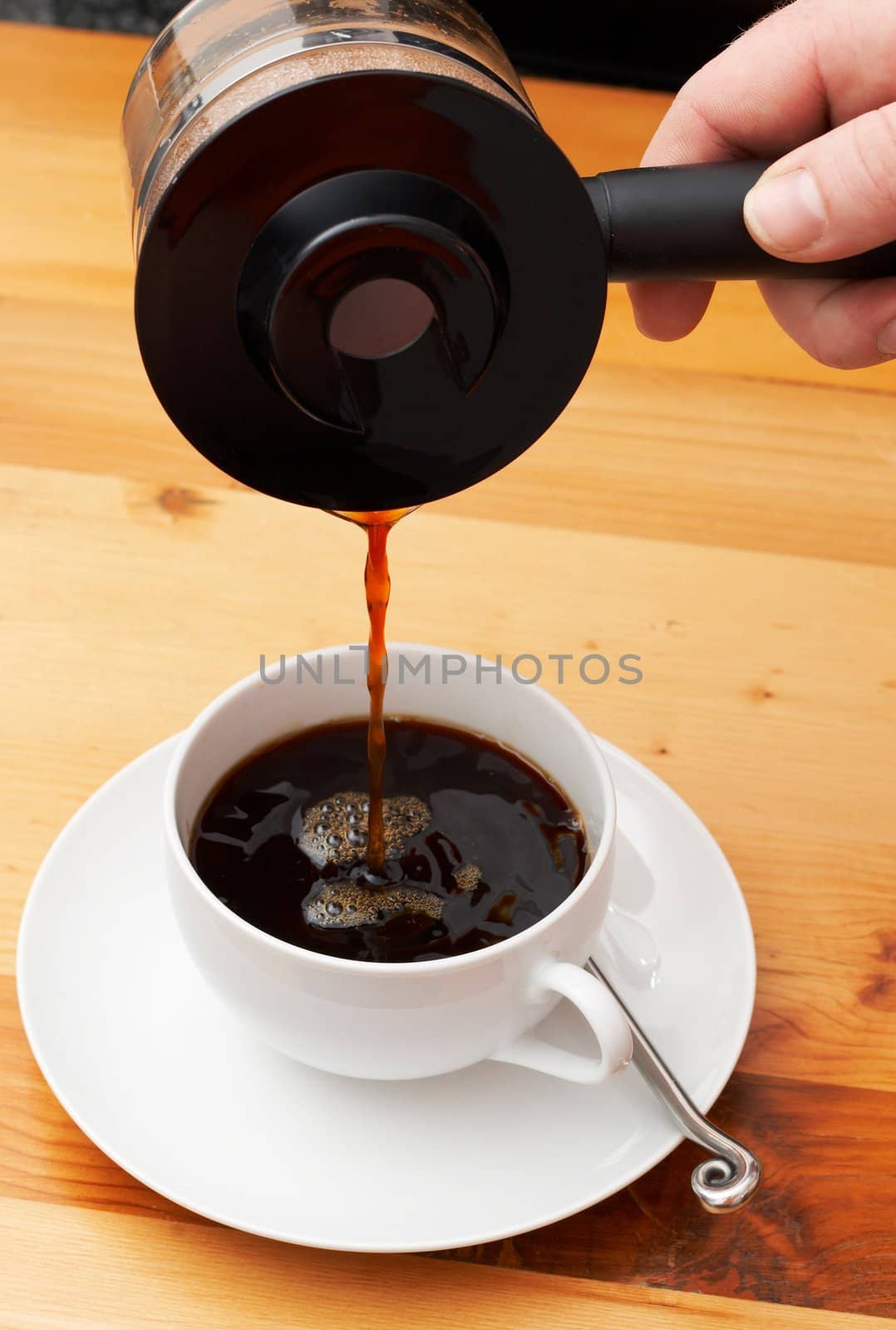 Closeup of coffee being poured from the pot into the cup. Shot on light wood background