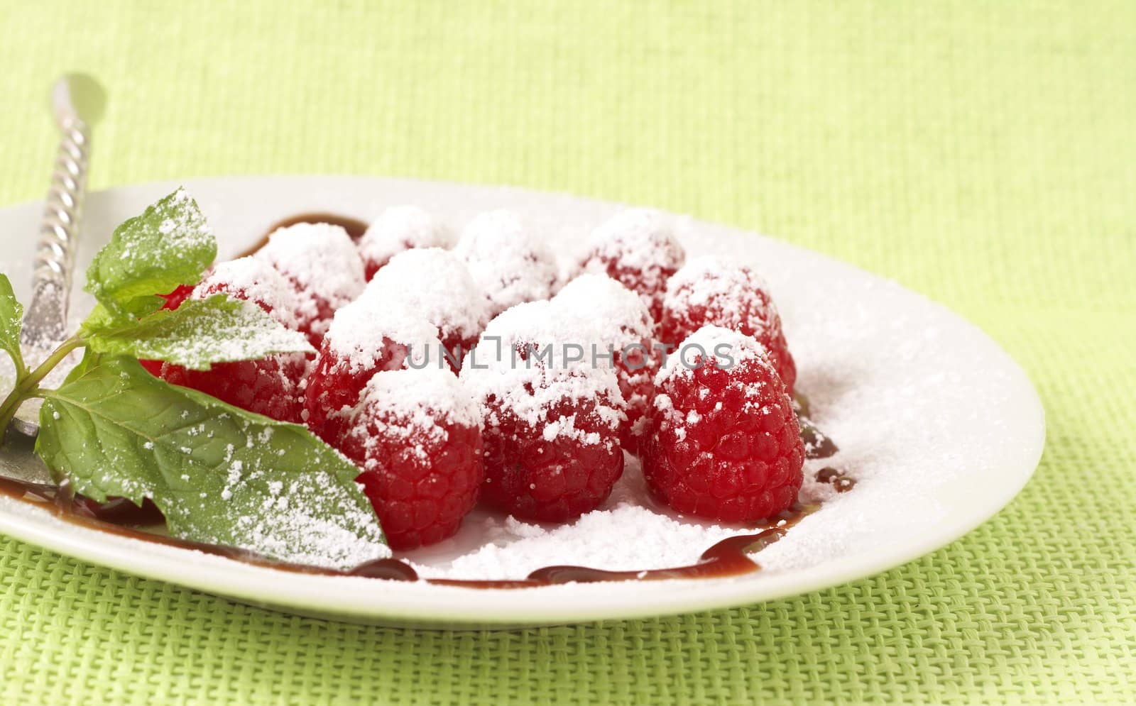 Fresh raspberry dessert served on a white plate, garnished with mint, chocolate sauce and icing sugar
