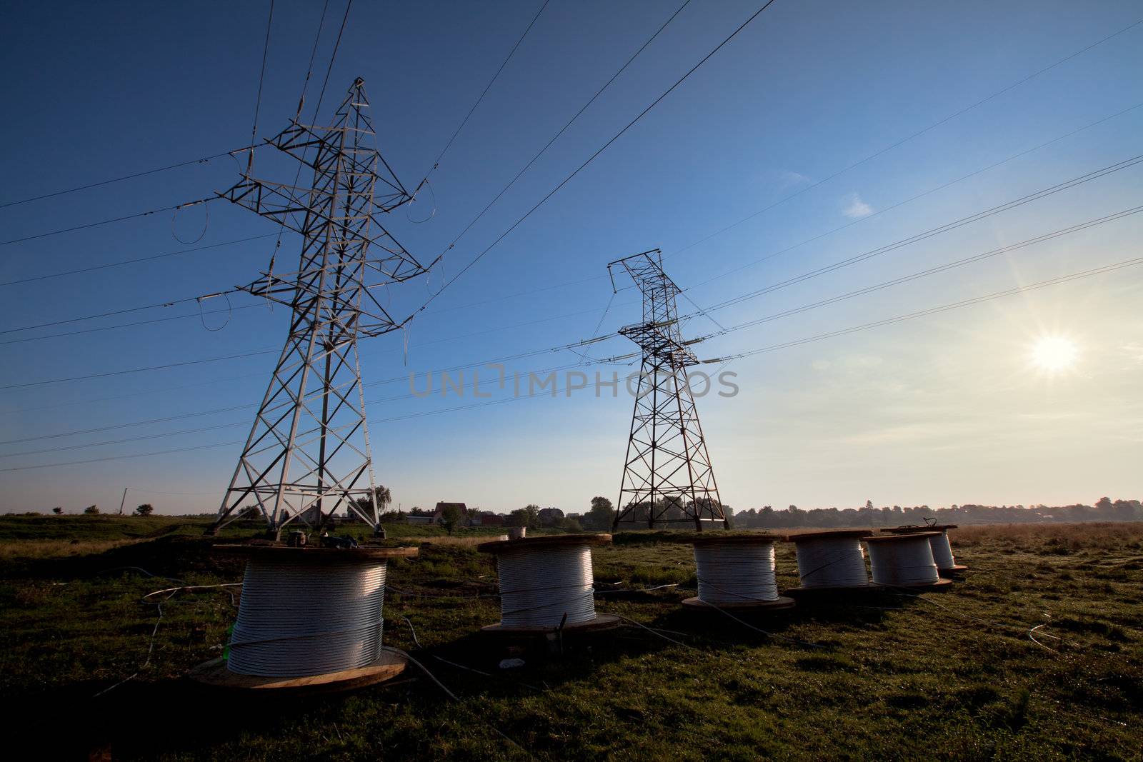 A power line tower in the field and six bobbins with aluminum wire ready to installation