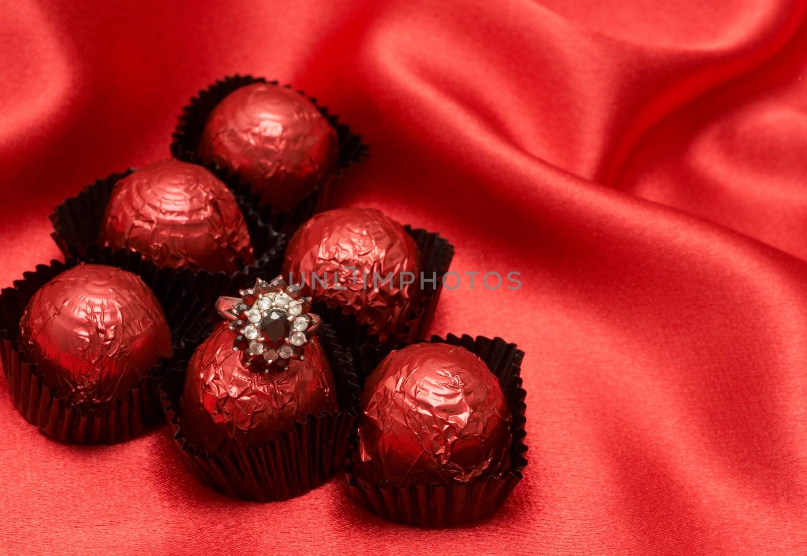 Valentines chocolate truffles with an expensive engagement ring shot on red silk background