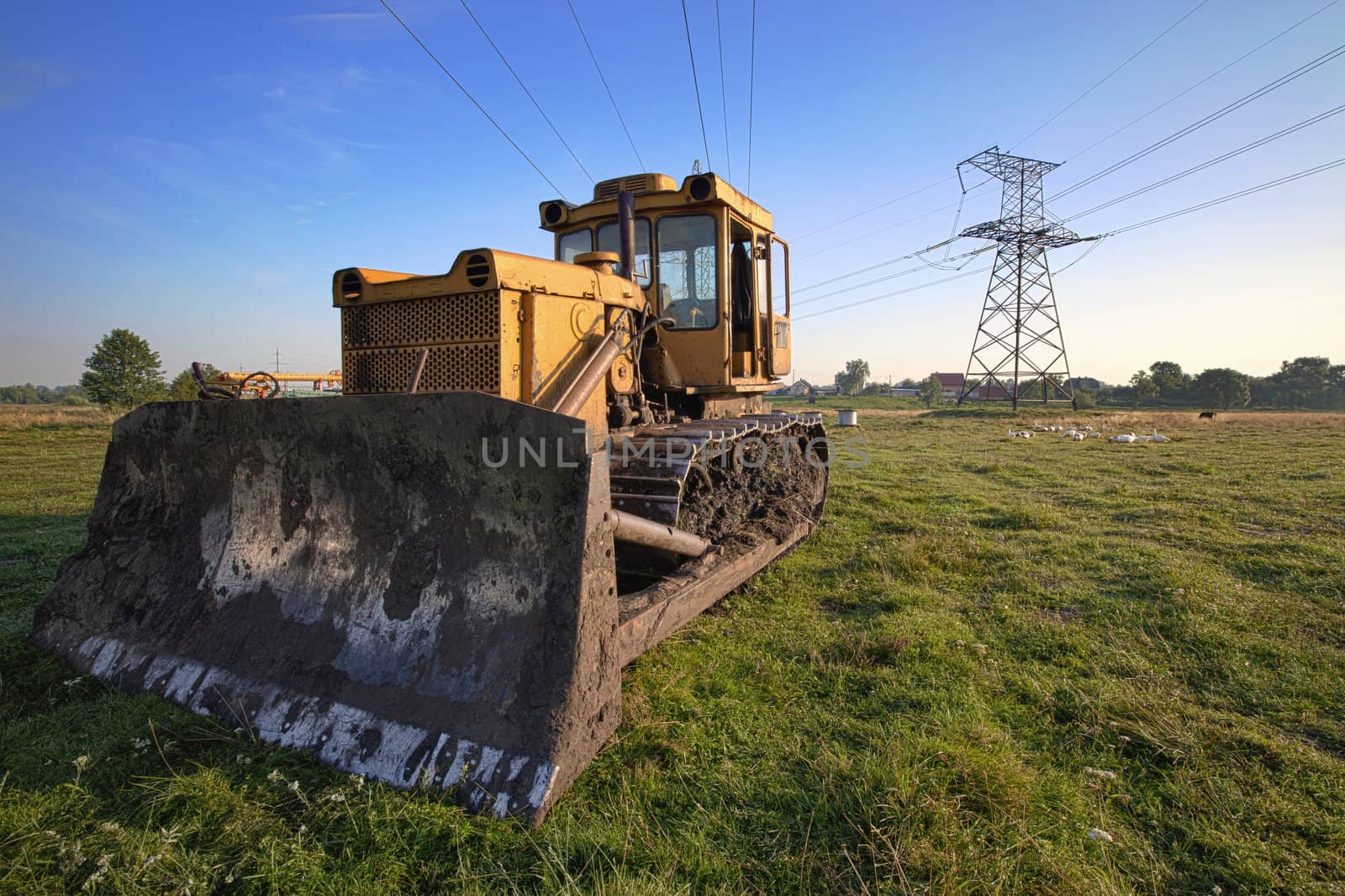 Old dirty yellow bulldozer in front of power lines towers over the blue sky