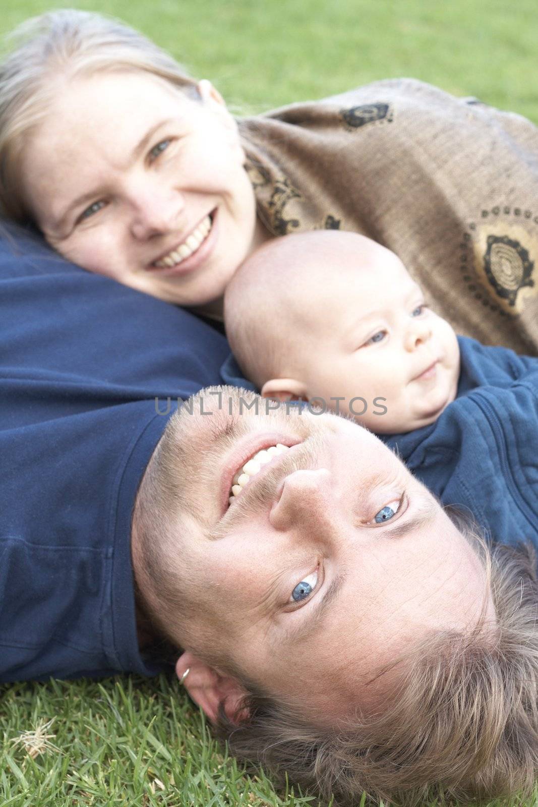 Beautiful happy family of three lying on the grass laughing. Focus is on the father