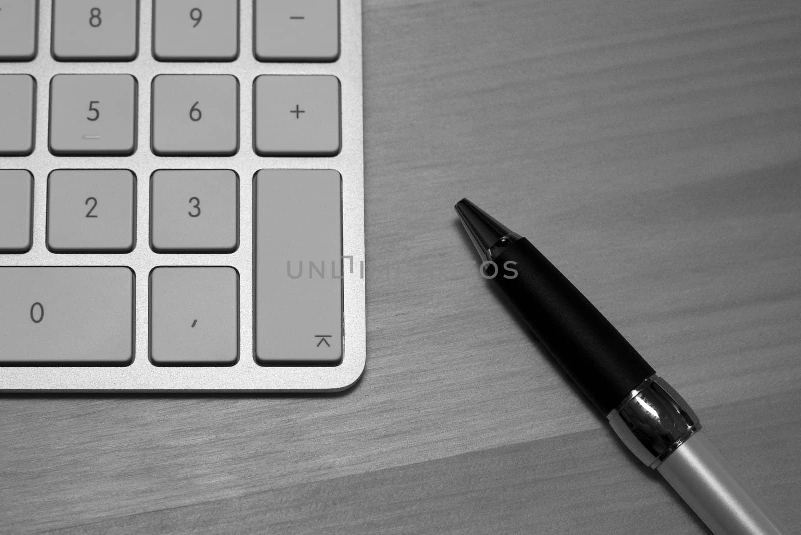 greyscale picture of keyboard and pen on wood