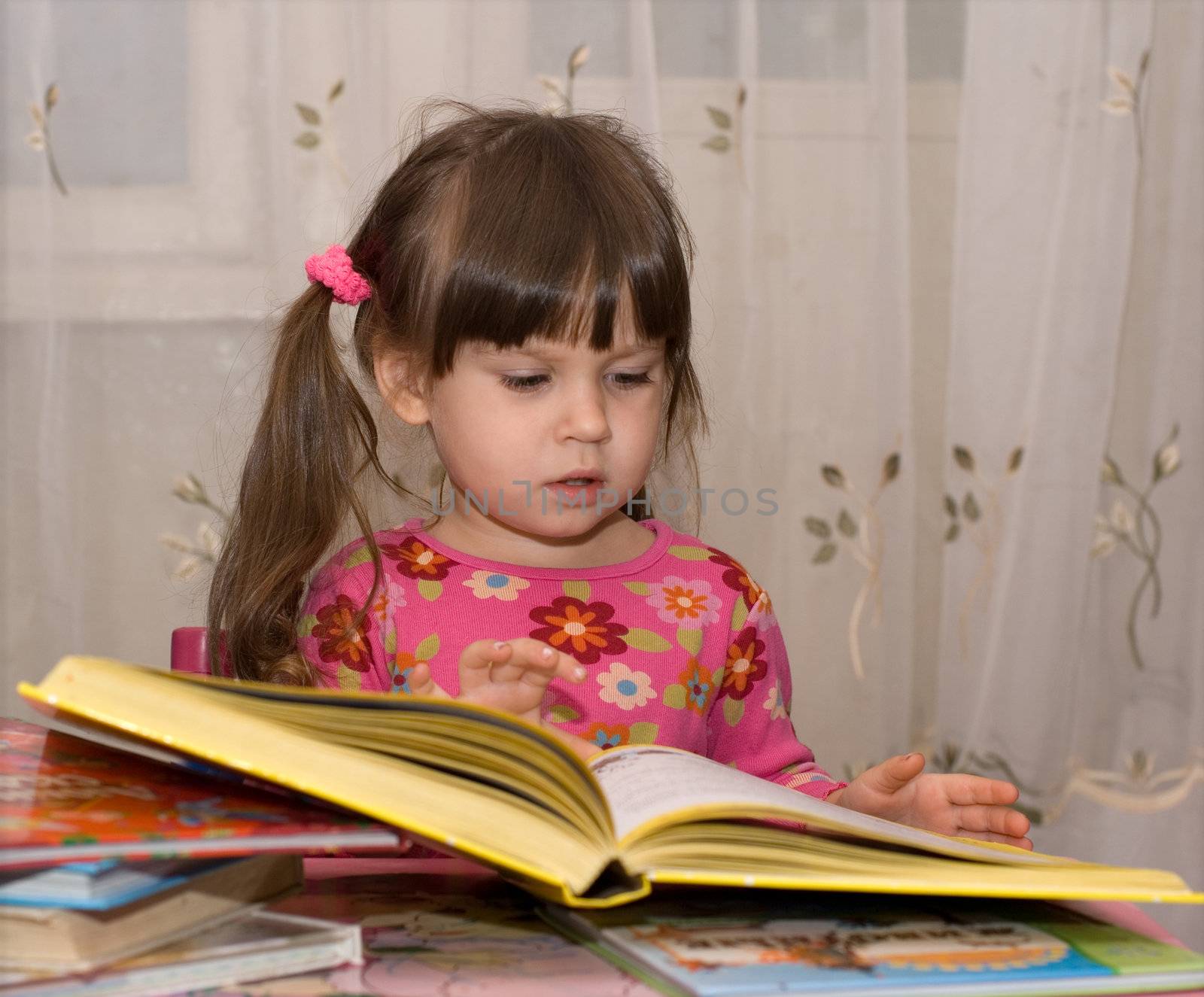 The child reading the book. The three-year girl in house conditions