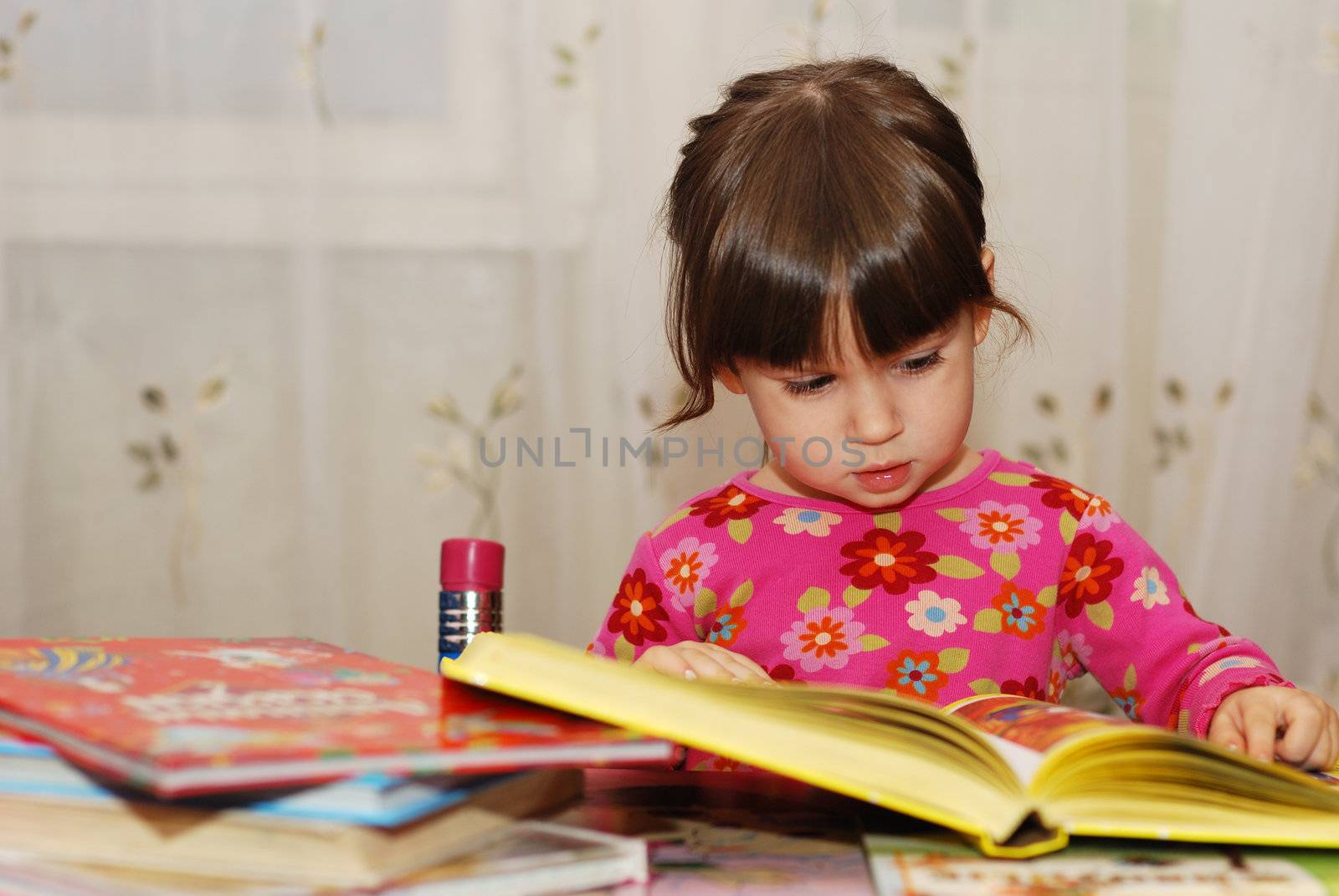 The child reading the book. The three-year girl in house conditions