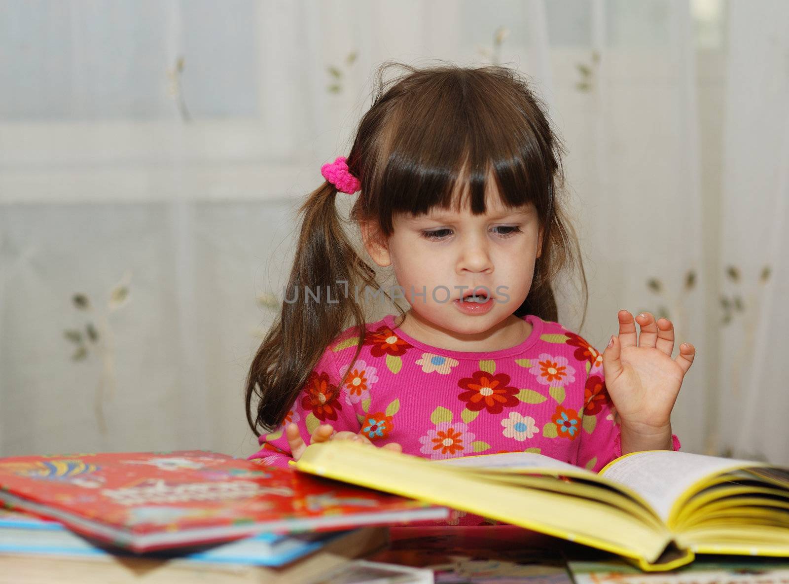 The child reading the book. The three-year girl in house conditions