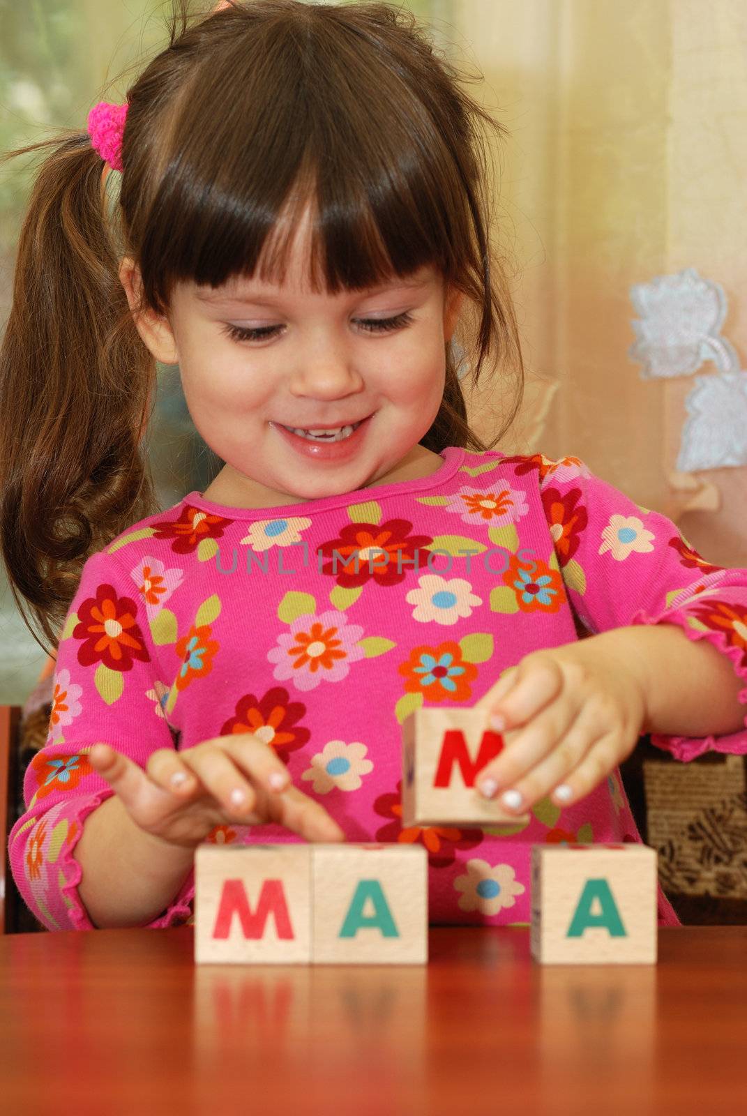 The girl and toy cubes. The child collecting a word mama from cubes.