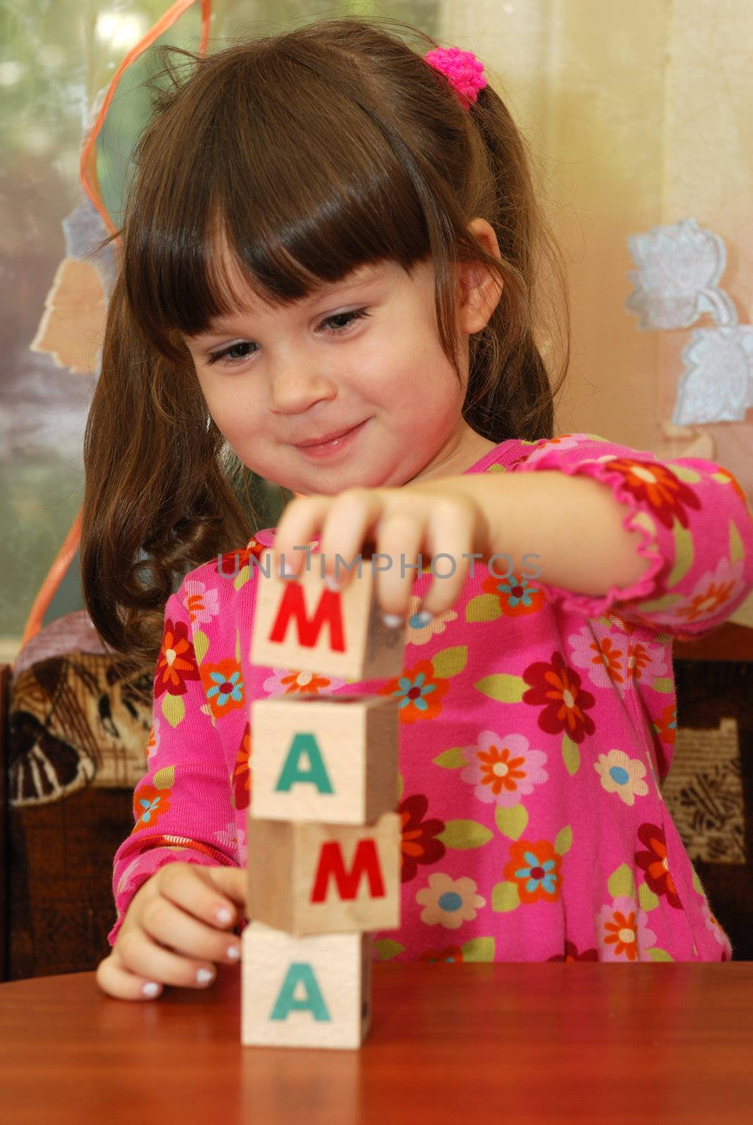 The girl and toy cubes. The child collecting a word mama from cubes.