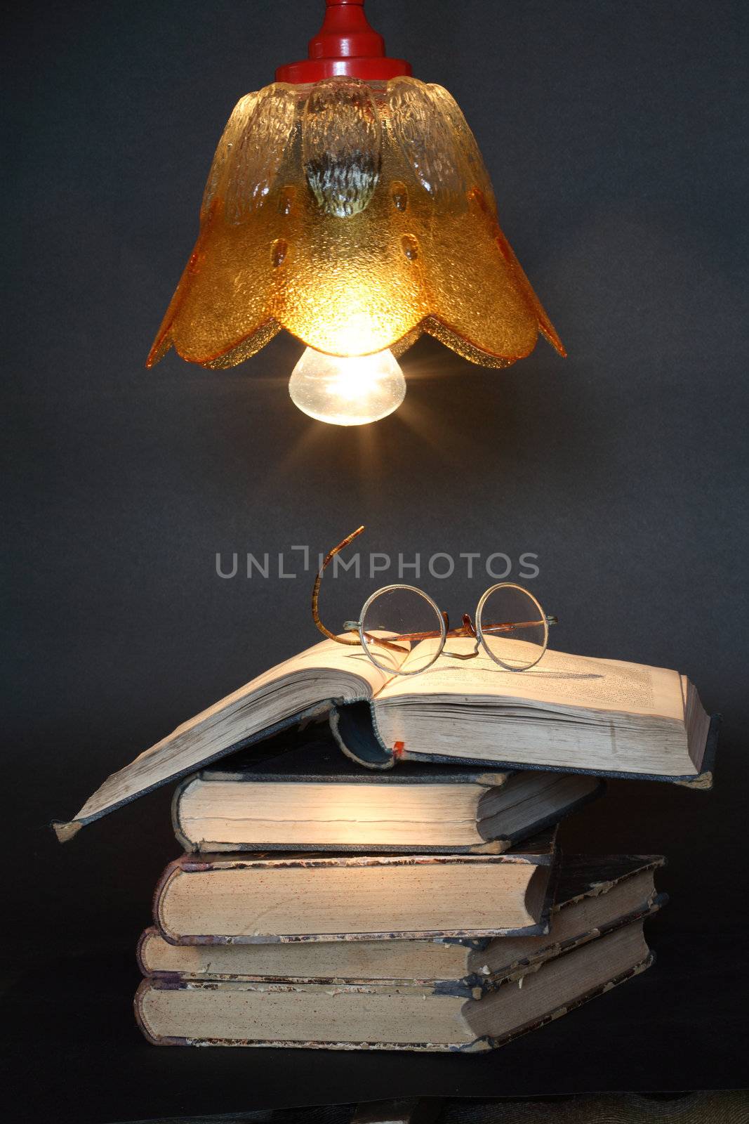 Stack of old books and spectacles under luminous lamp