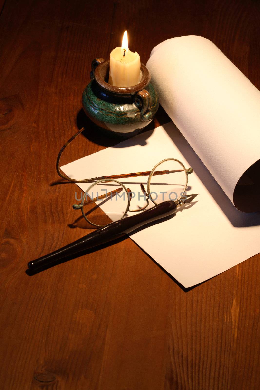 Scroll and old spectacles near lighting candle on wooden surface