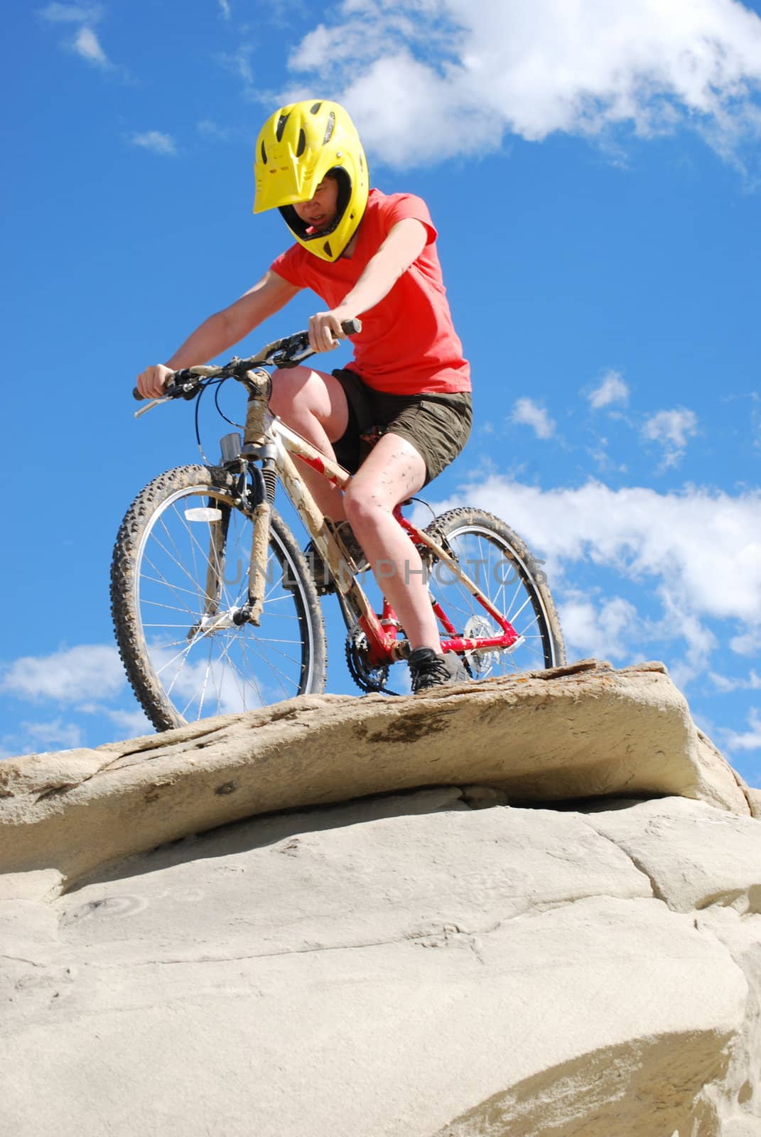 Mountain biker in red and orange against boulders and blue sky.