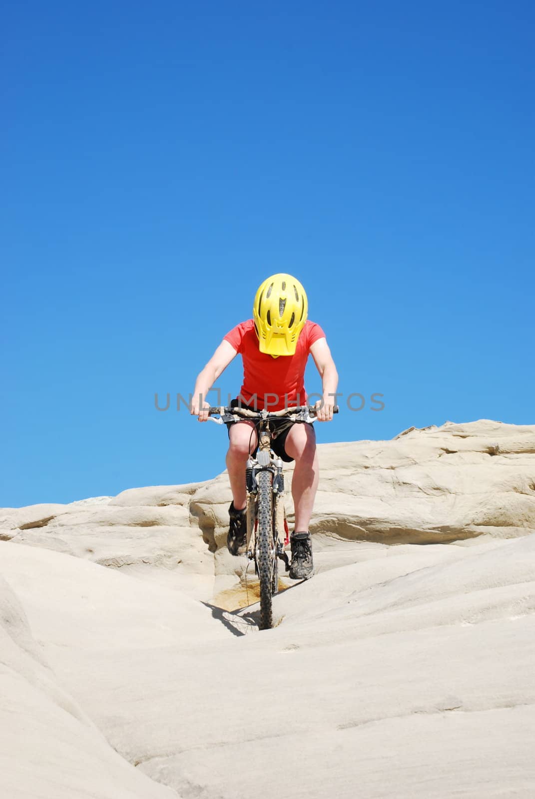 Mountain biker in red and orange against boulders and blue sky.