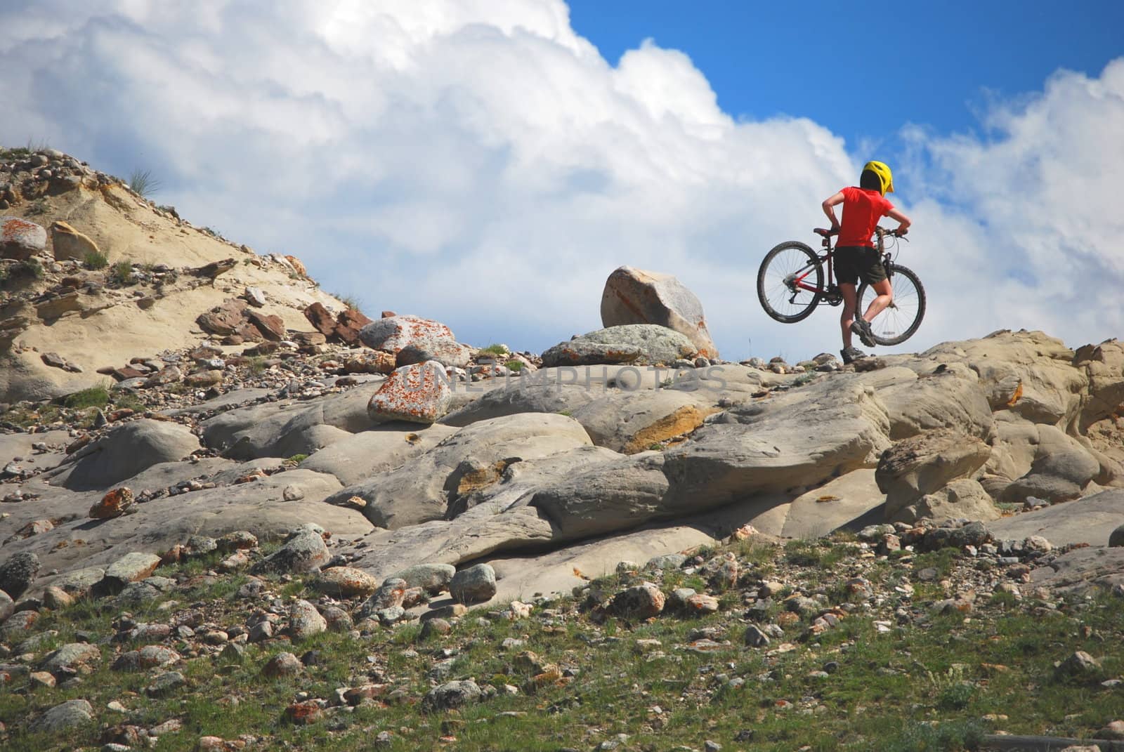 Mountain biker in red and orange against boulders and blue sky.