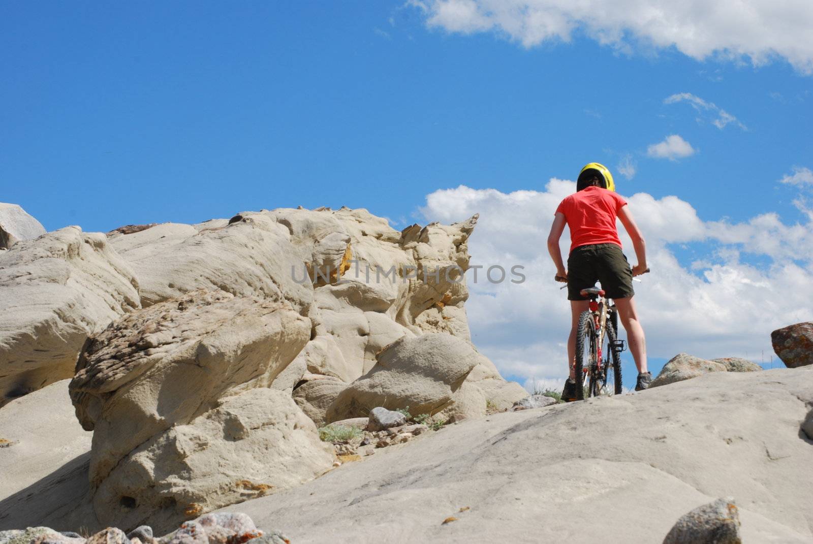 Mountain biker in red and orange against boulders and blue sky.