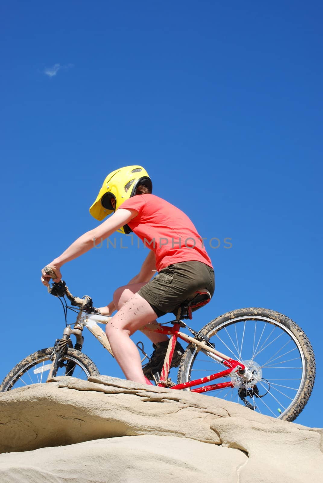 Mountain biker in red and orange against boulders and blue sky.