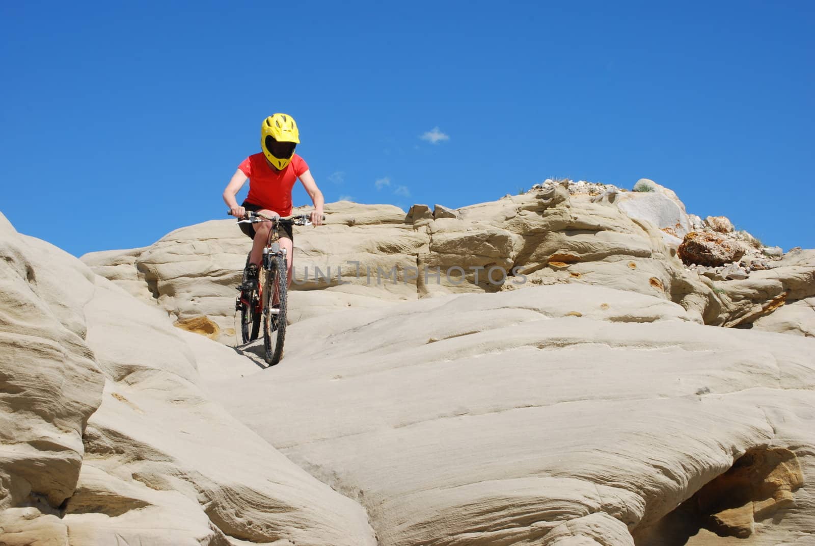 Mountain biker in red and orange against boulders and blue sky.