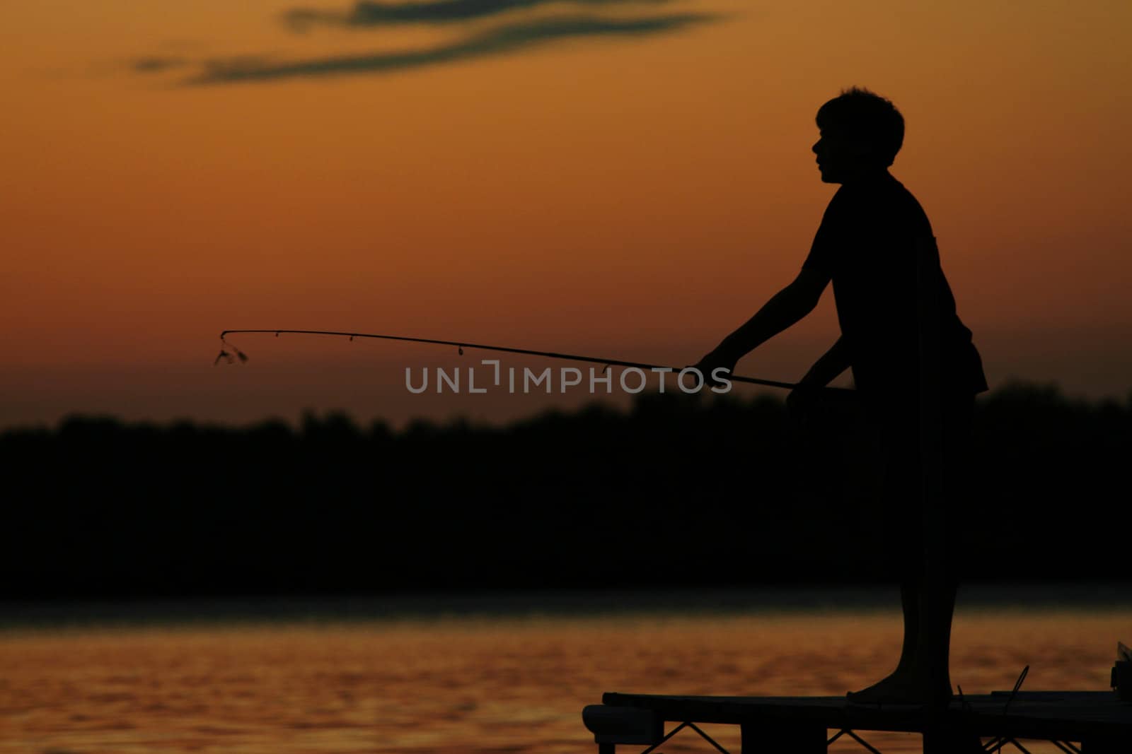 Silhouette of boy fishing off pier at sunset by jarenwicklund