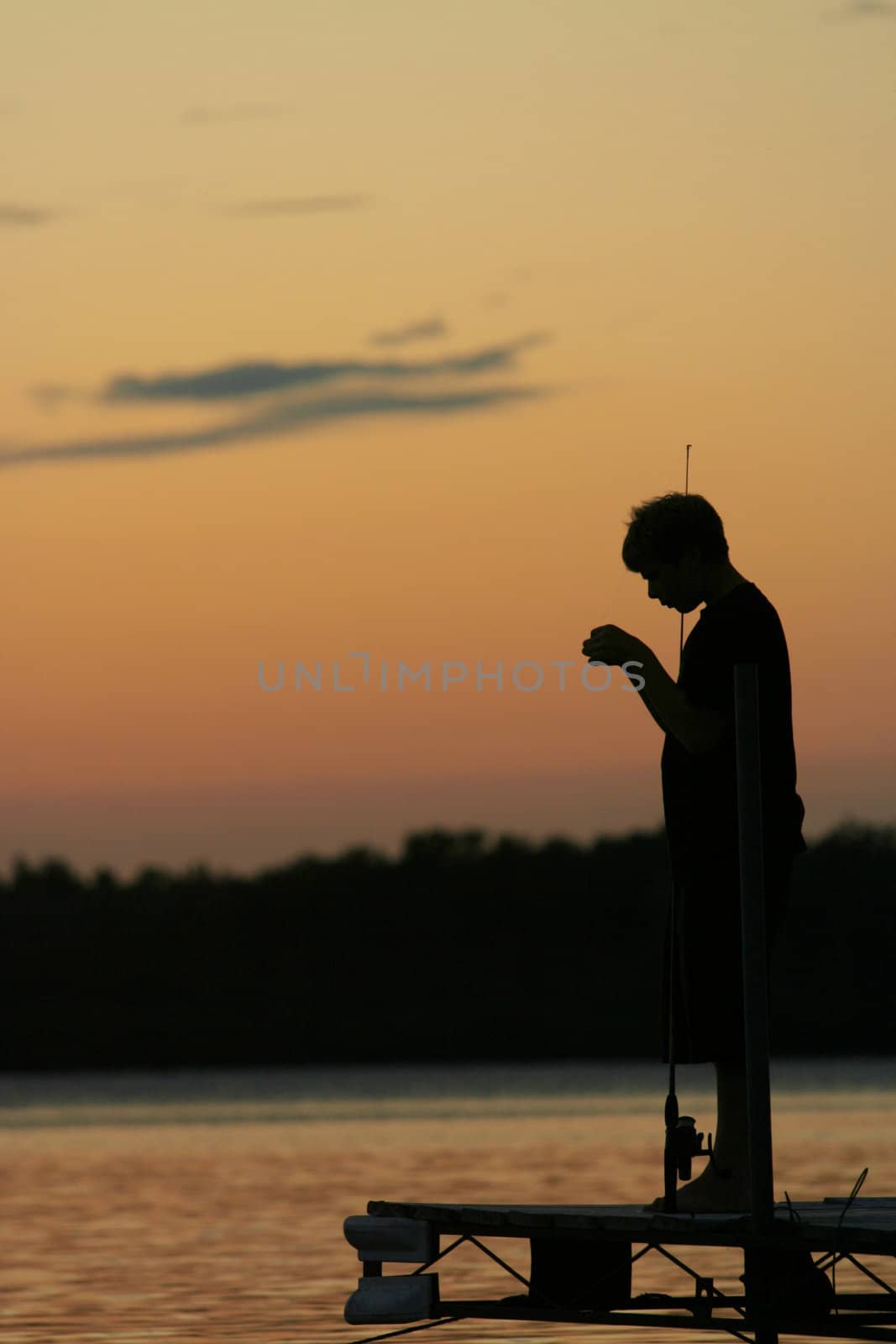 Silhouette of boy fishing off pier at sunset