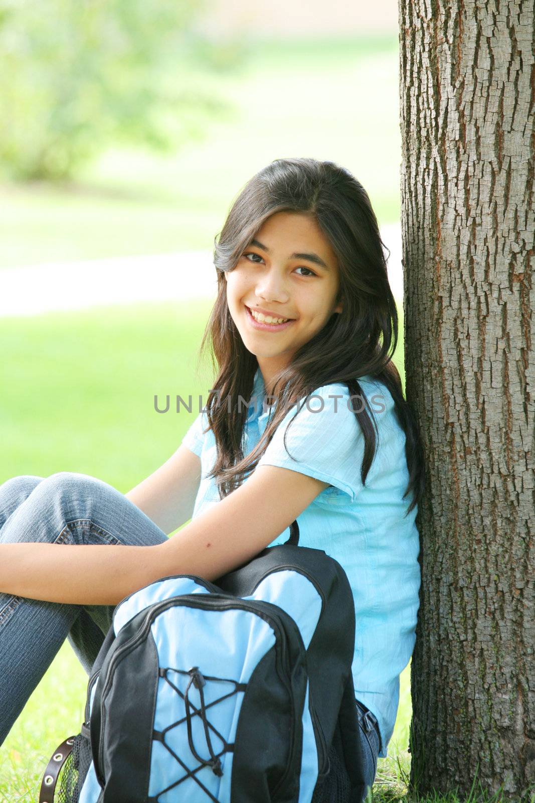 Young teen girl sitting against tree with backpack. Part Asian, Scandinavian background.