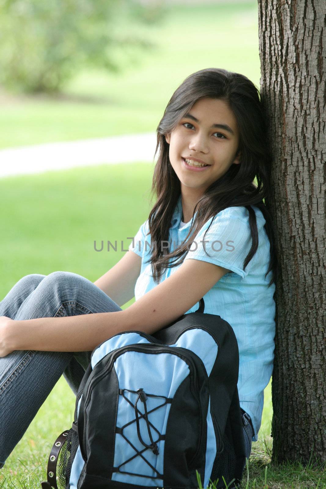 Young teen girl sitting against tree with backpack.  by jarenwicklund